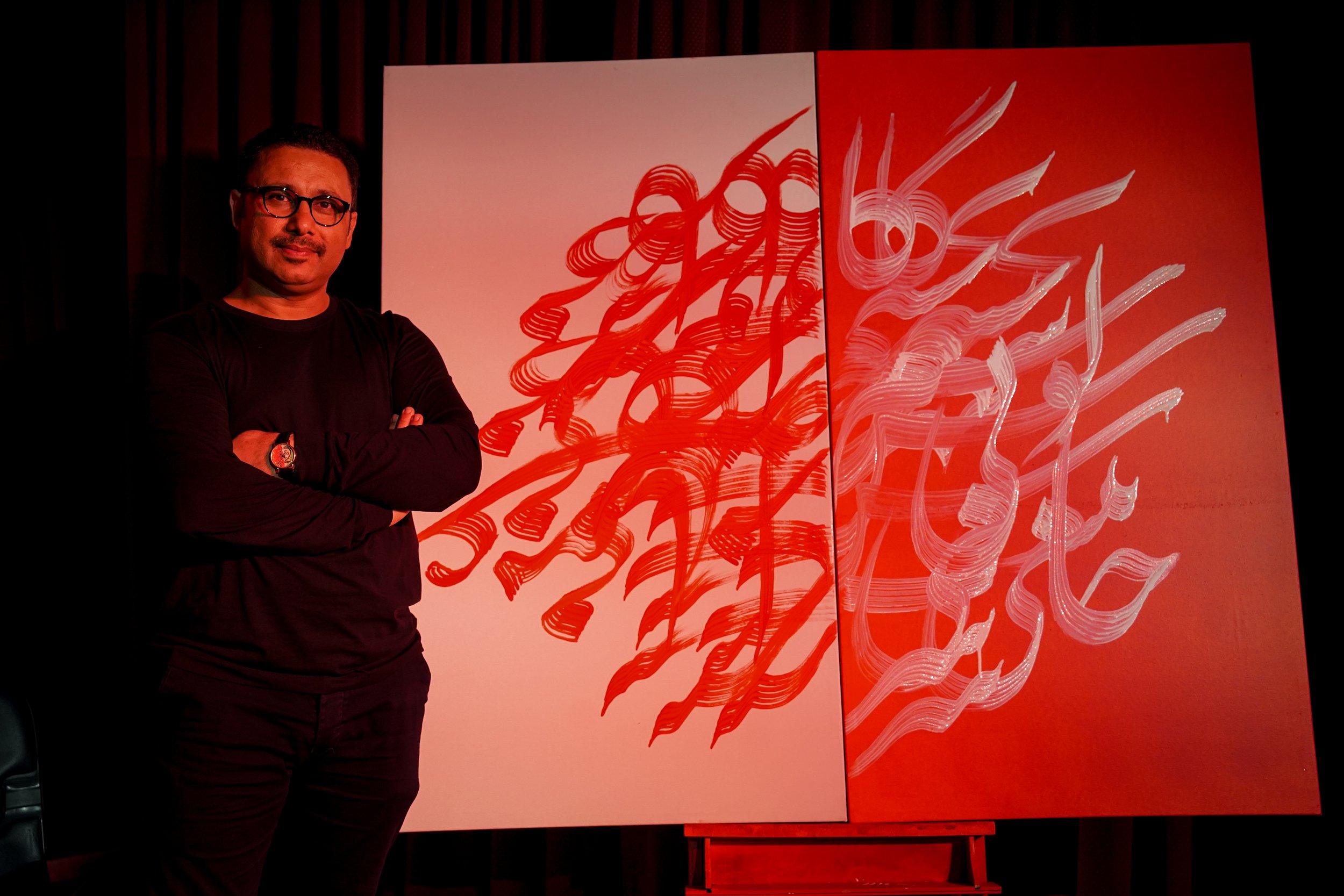 Person standing next to a painting with red and white abstract calligraphy on two panels.