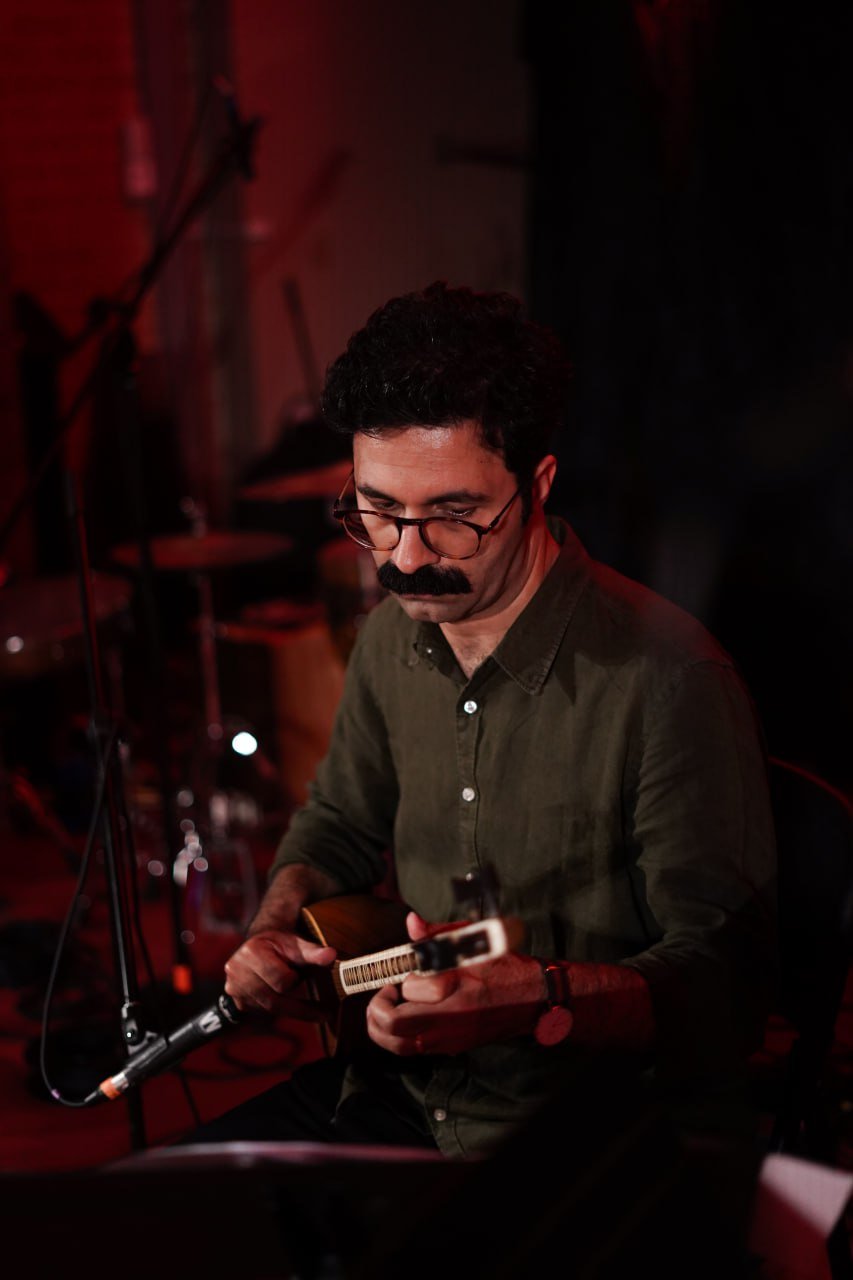 A musician playing a string instrument, with a microphone nearby, in a dimly lit setting.
