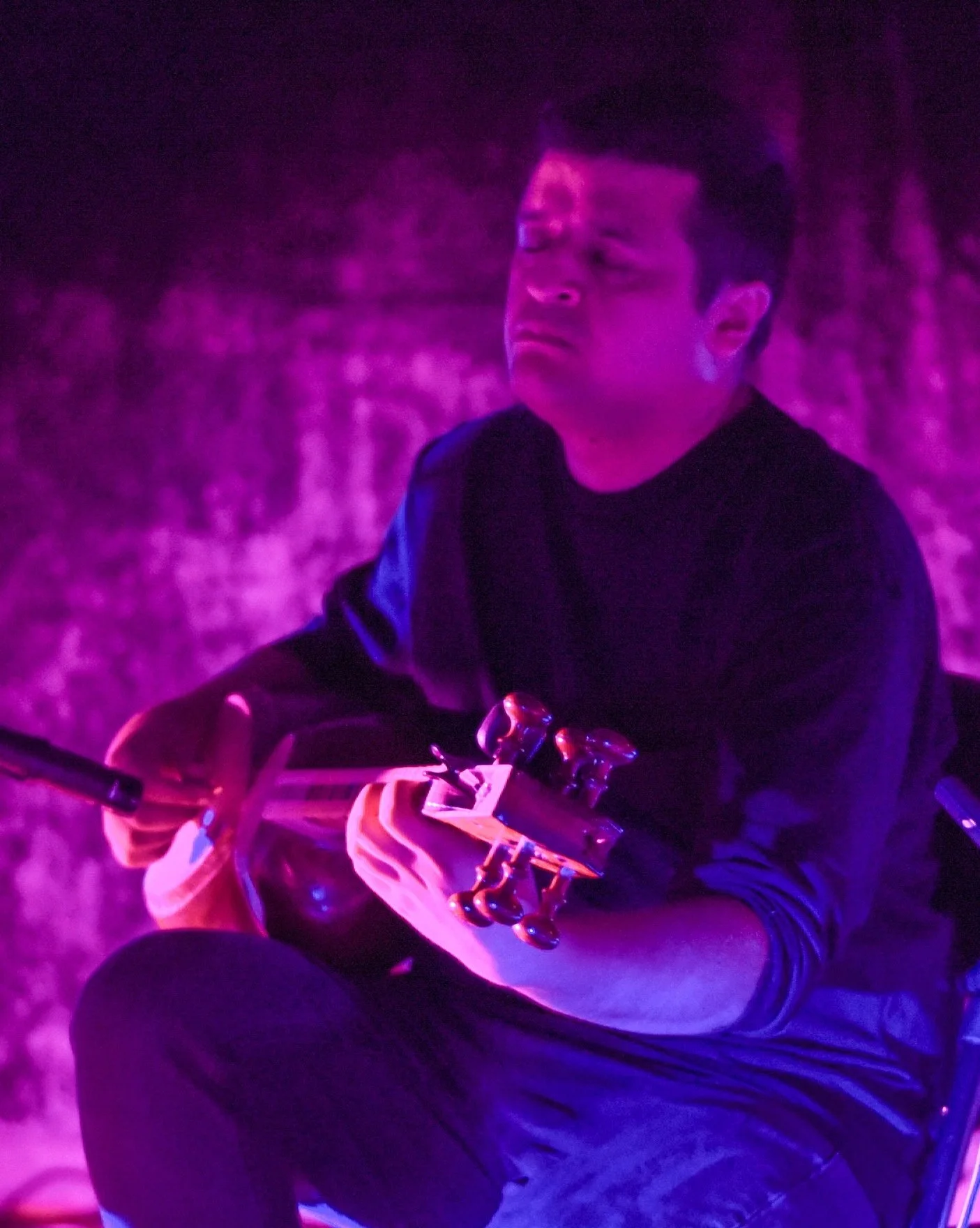 Person playing a string instrument under purple lighting.