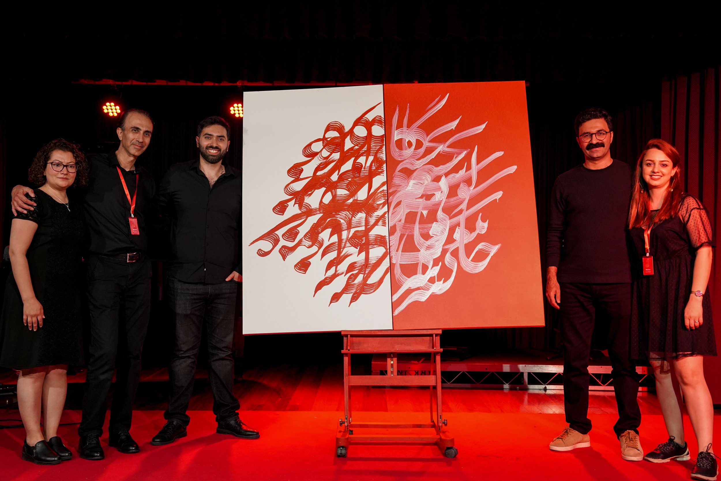 Five people standing on a stage with a two-panel artwork displaying abstract calligraphy, featuring red and white colors.
