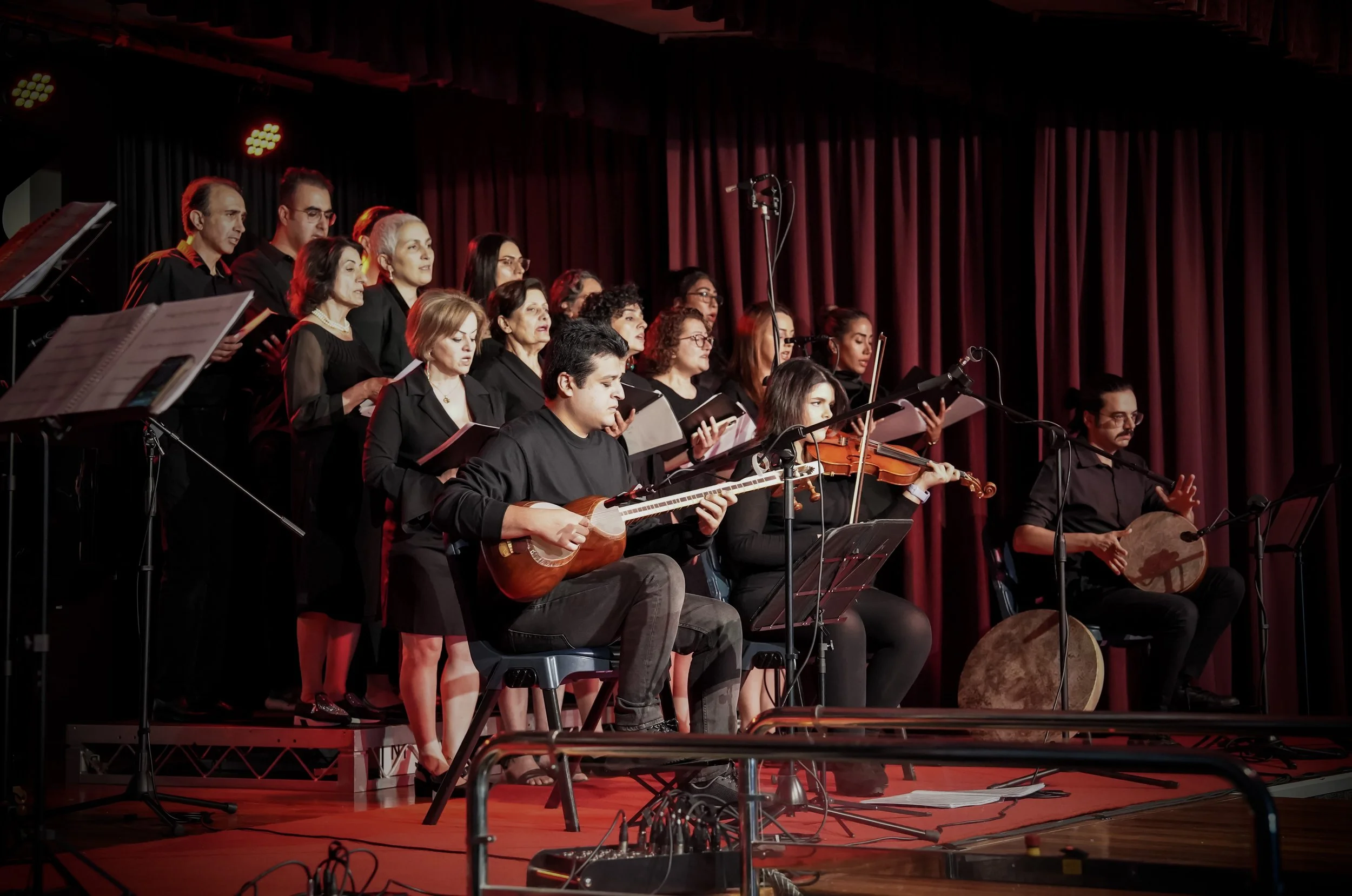Choir and musicians performing on stage with instruments and sheet music, illuminated by stage lights and surrounded by curtains.