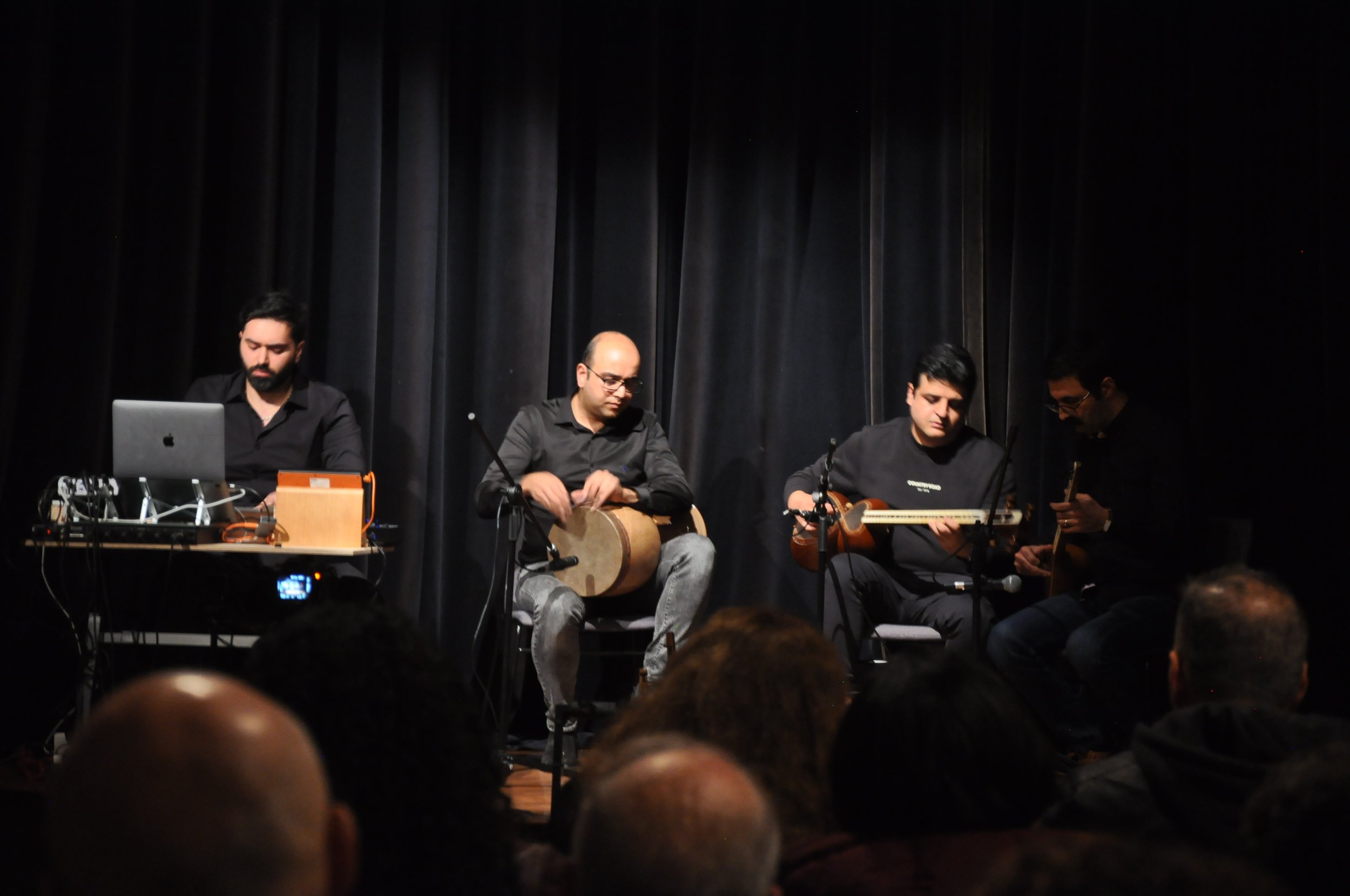 Musicians performing on stage with electronic equipment and traditional instruments.