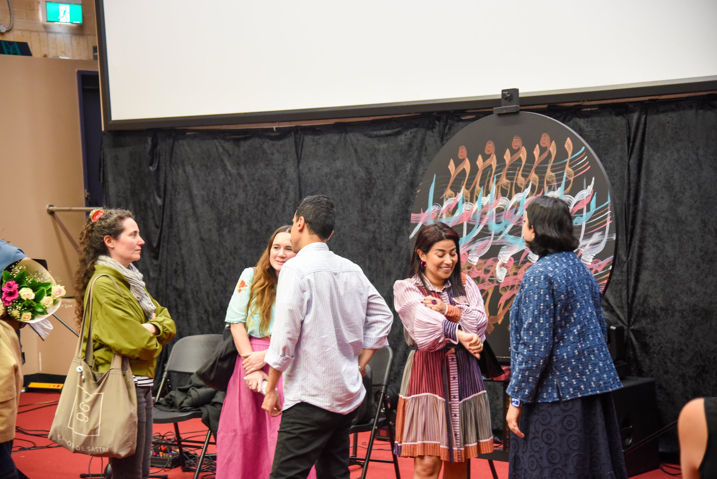 Group of people talking in a room with a large circular artwork and black curtain backdrop.