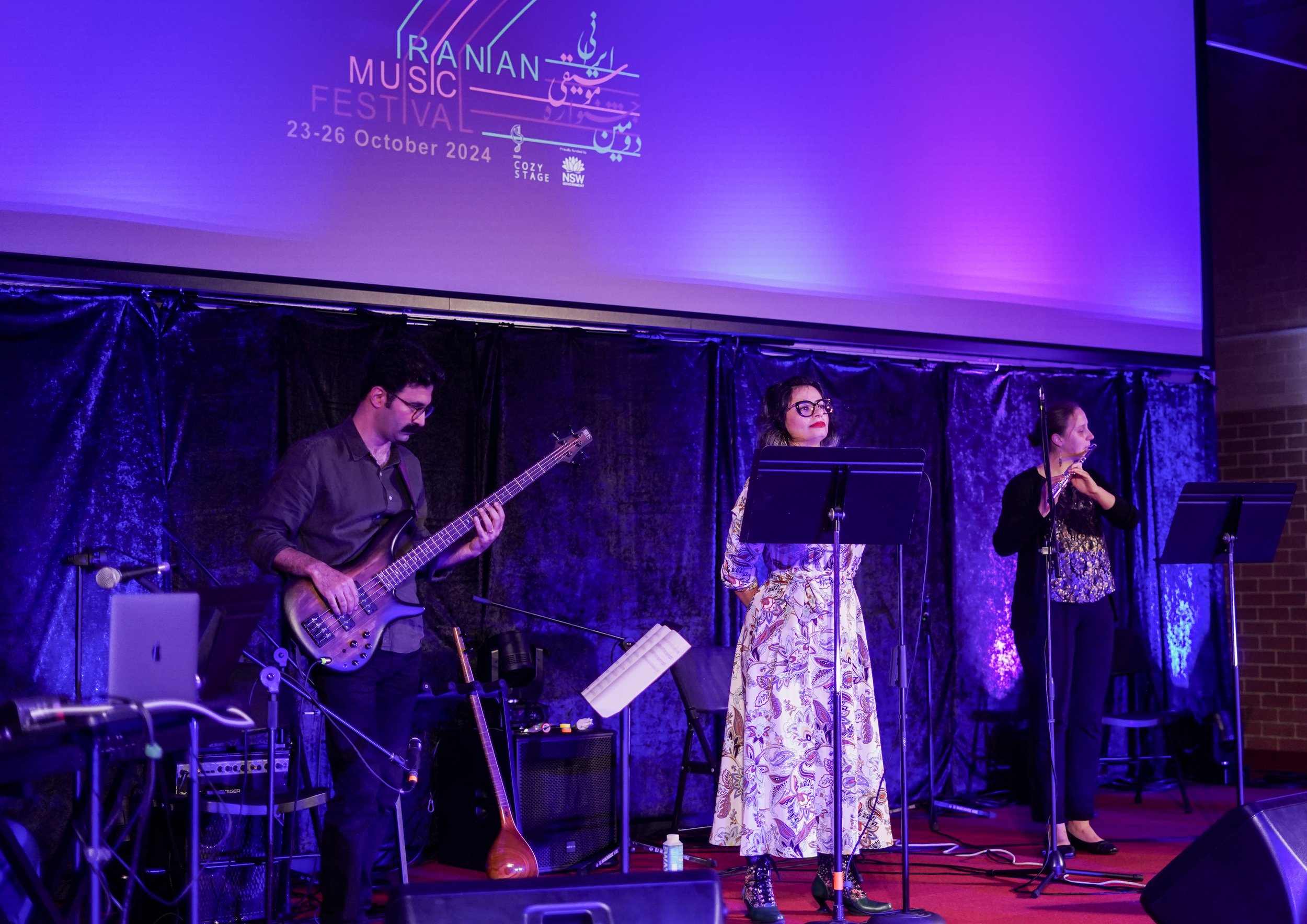 Musicians performing at the Iranian Music Festival with instruments and microphones on stage with purple lighting.