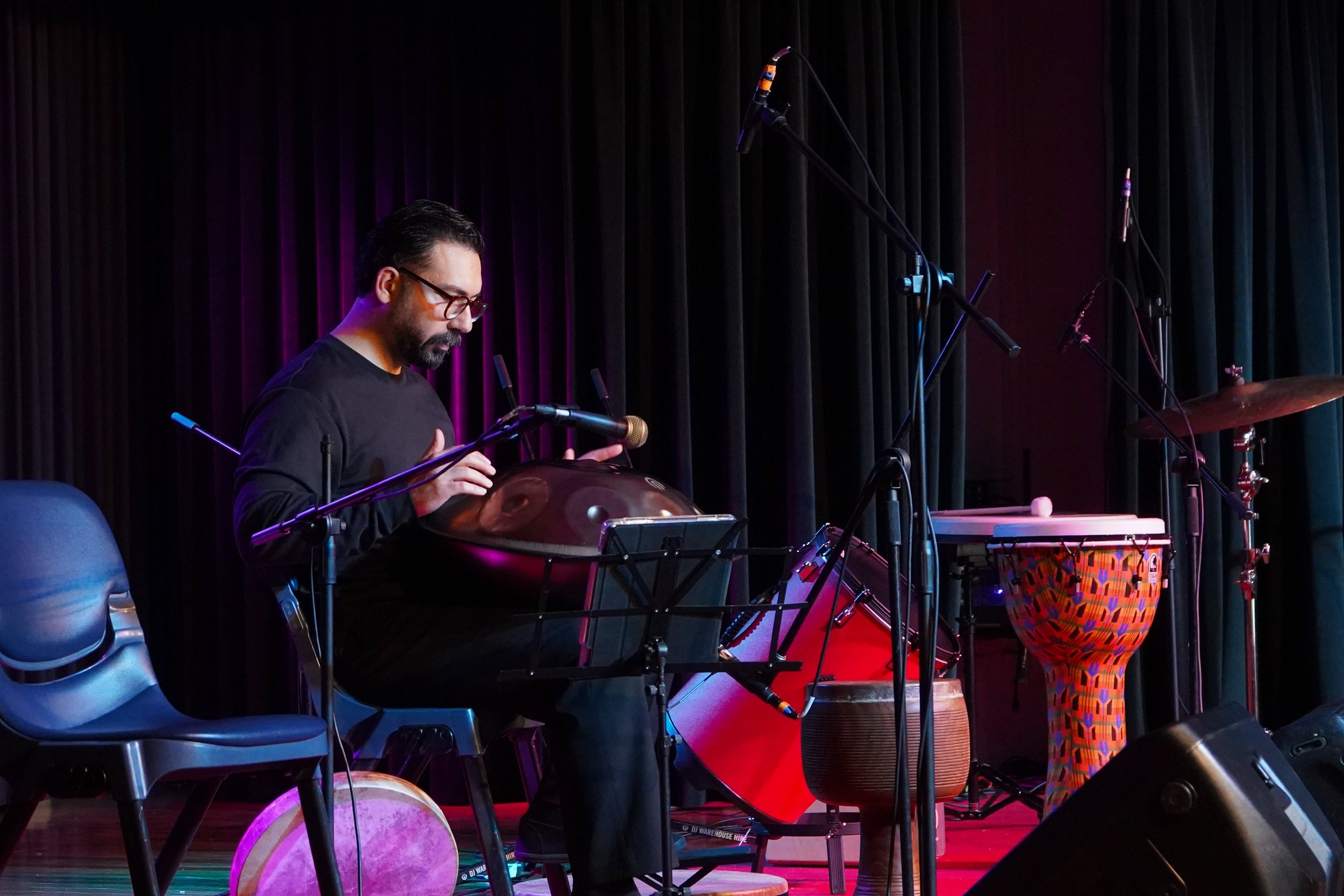 Musician playing hang drum on stage with percussion instruments