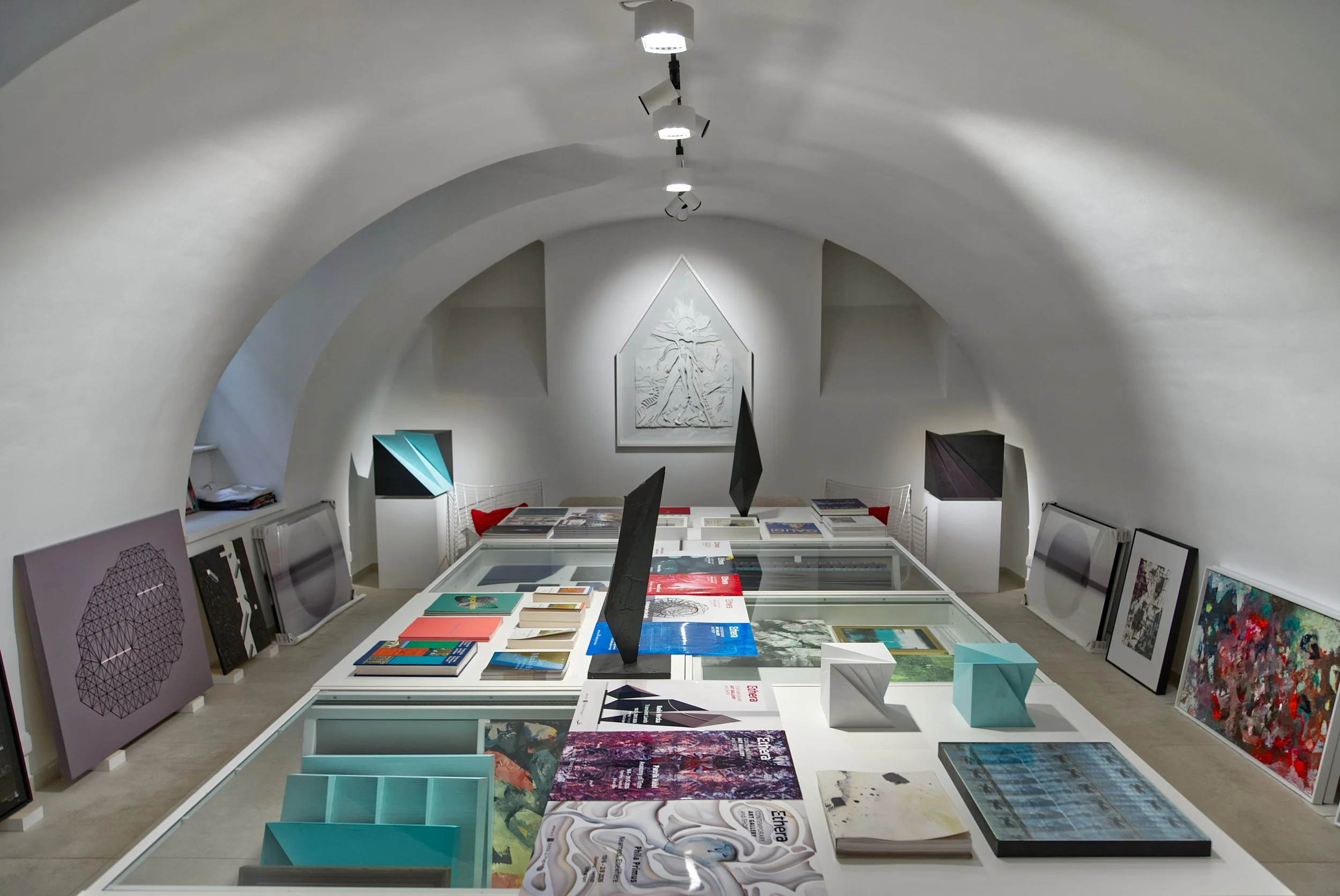 Modern minimalist gallery interior with white arched ceiling, overhead lighting, and display cases.