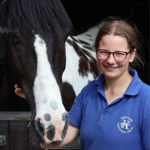 A young girl with glasses and a blue shirt smiling next to a black and white horse.