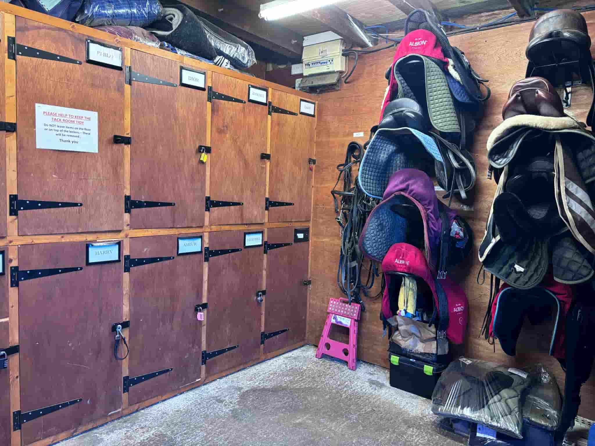 Wooden lockers with various locked compartments and labels, with sports equipment, shoes, and backpacks stored nearby in a locker room.