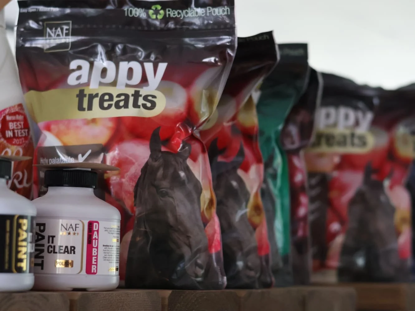 Shelf with bags of Happy Treats horse treats, featuring a black horse on the packaging, and bottles of equine supplements including A Mint Pain and Default Deuber.