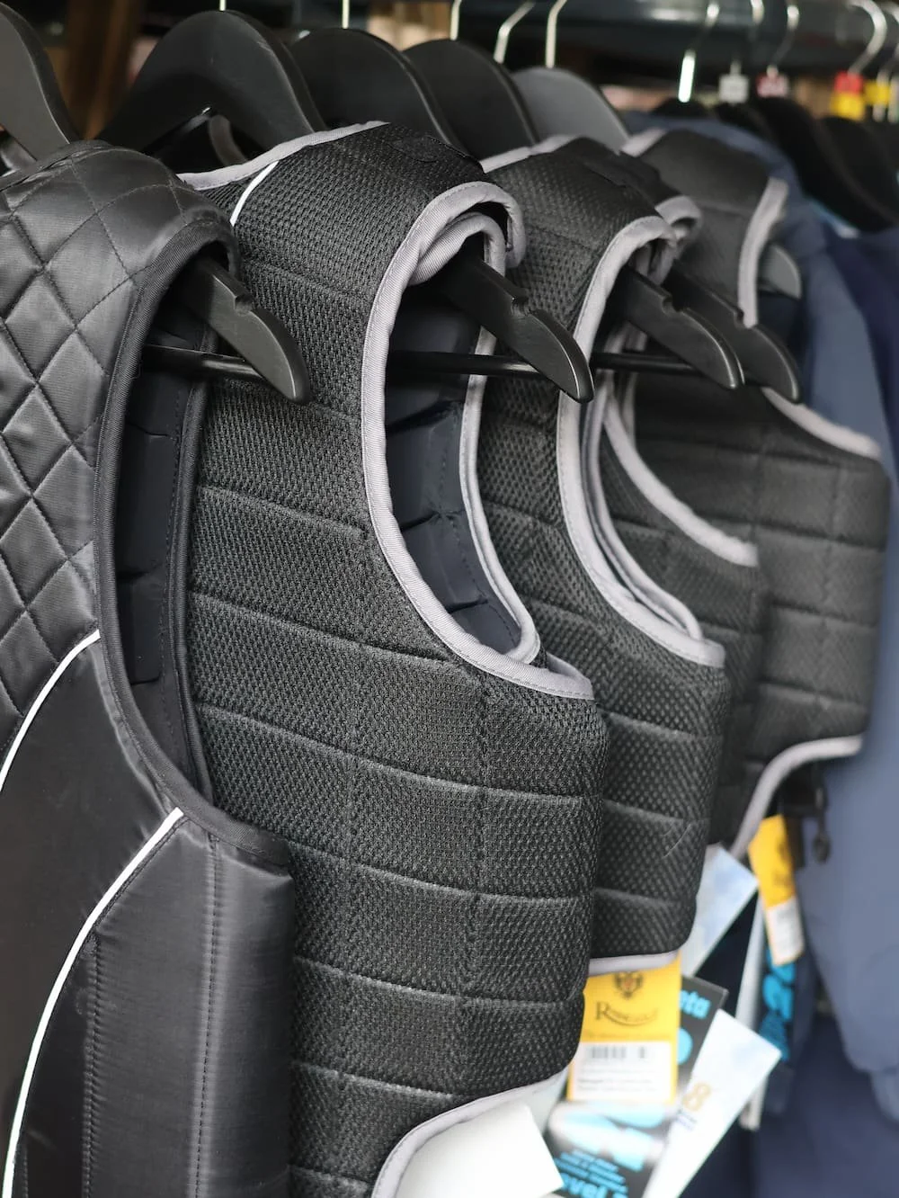 Several black padded life vests hanging on store hooks.