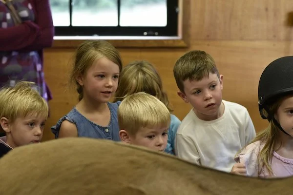 A group of young children, both boys and girls, are gathered and looking intently at something in front of them, with expressions of curiosity and attentiveness.