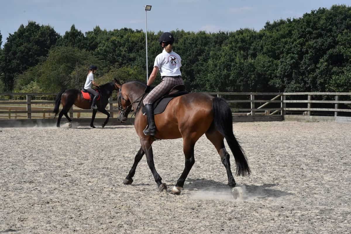 Two young girls riding horses in an outdoor riding arena.