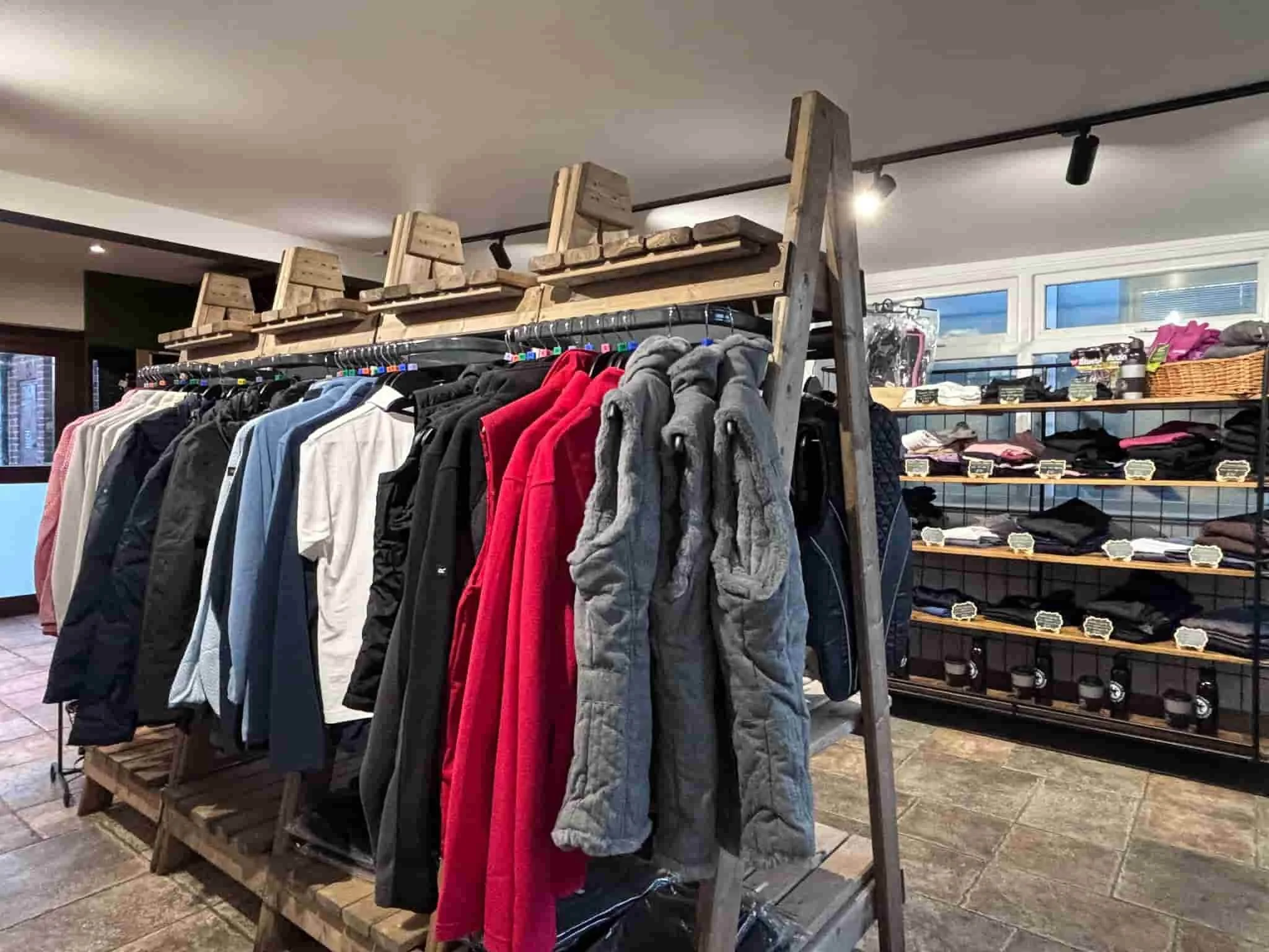Clothing store display with a metal rack holding jackets and hoodies, a wooden pallet used as a base, wooden crates on top, and shelves with folded clothes in the background.
