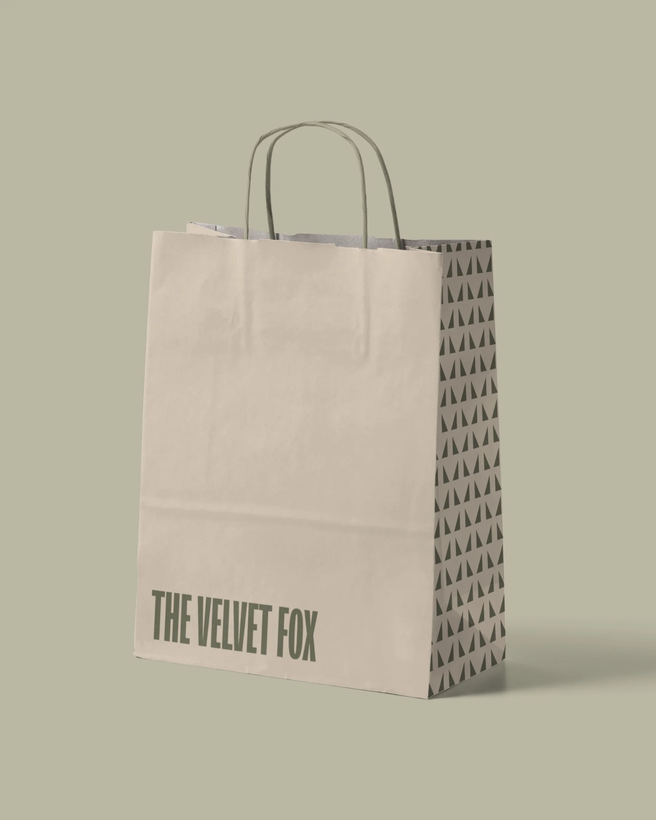 A shopping paper bag from The Velvet Fox with a pattern on the back and plain front with the store name in bold letters.