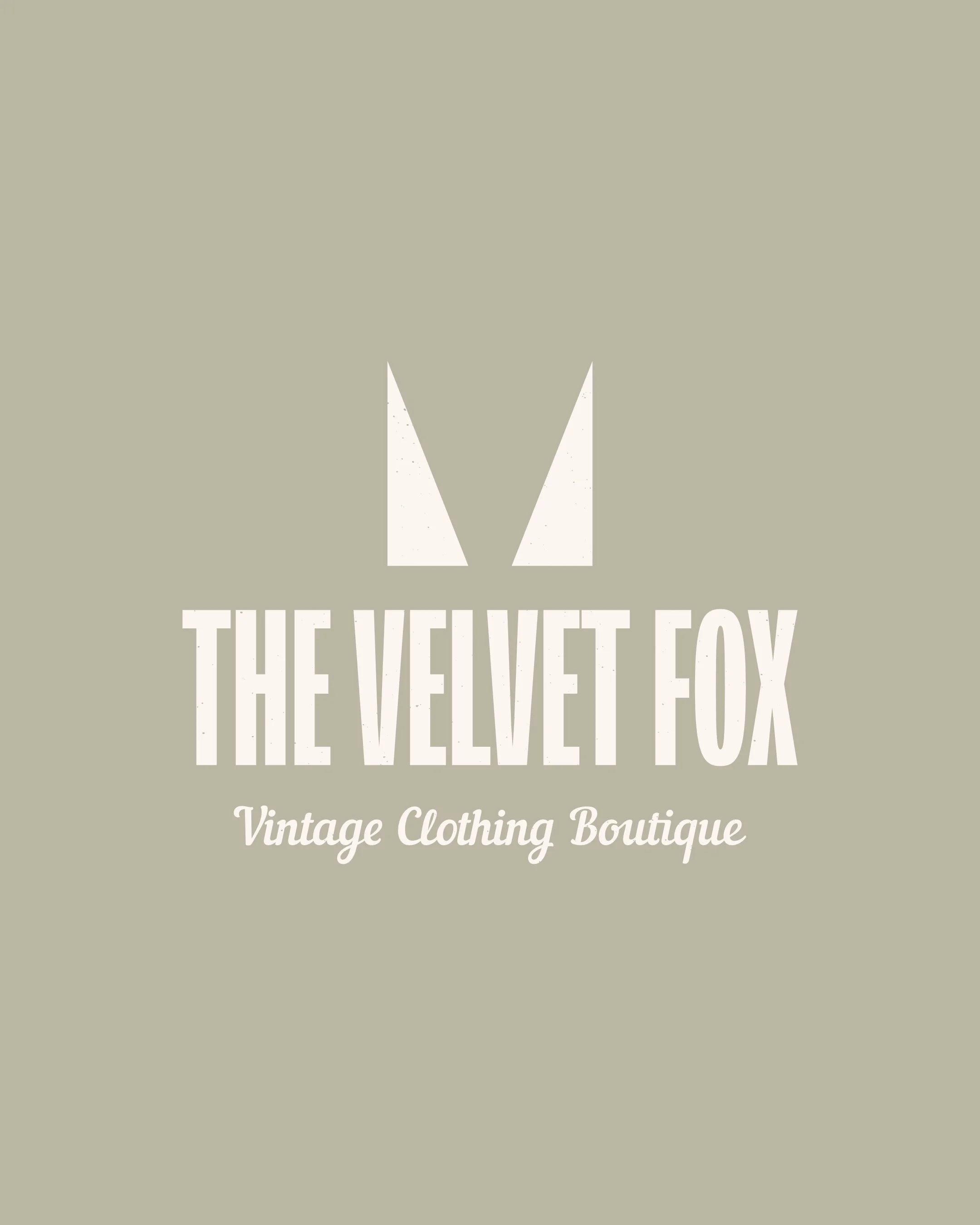 Vintage logo for The Velvet Fox, a clothing boutique, with stylized fox ears and the boutique's name in bold and cursive fonts on a light gray background.
