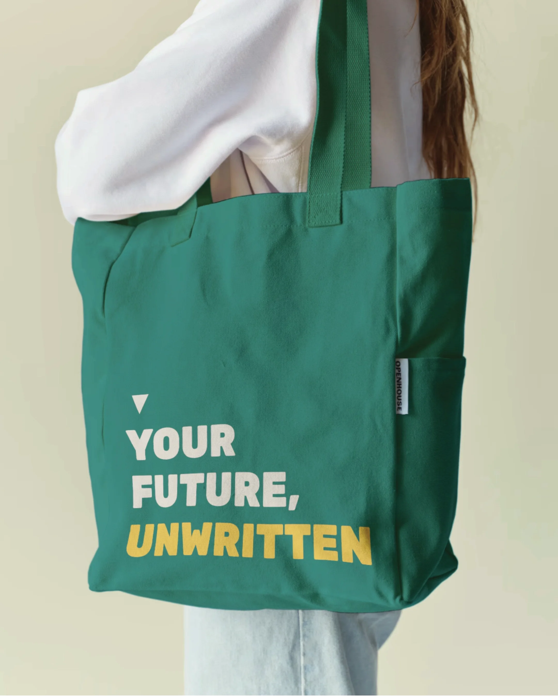 Green tote bag with white and yellow text reading 'Your Future, Unwritten', held by a person wearing a white jacket.