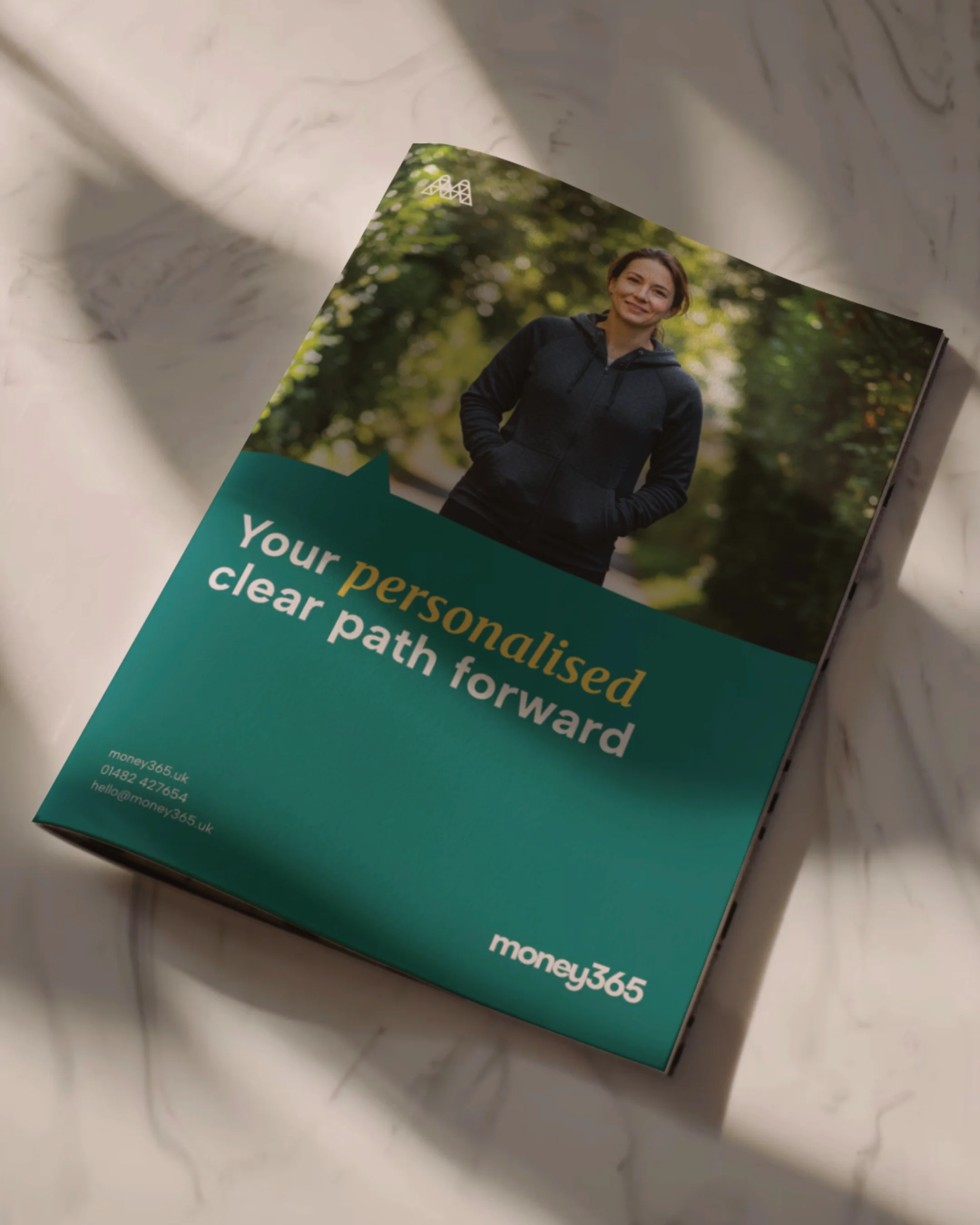 A brochure with a photo of a woman in a dark jacket standing outdoors with trees in the background. The brochure has green and teal colors with the text "Your personalized clear path forward" and contact information for money365.uk.