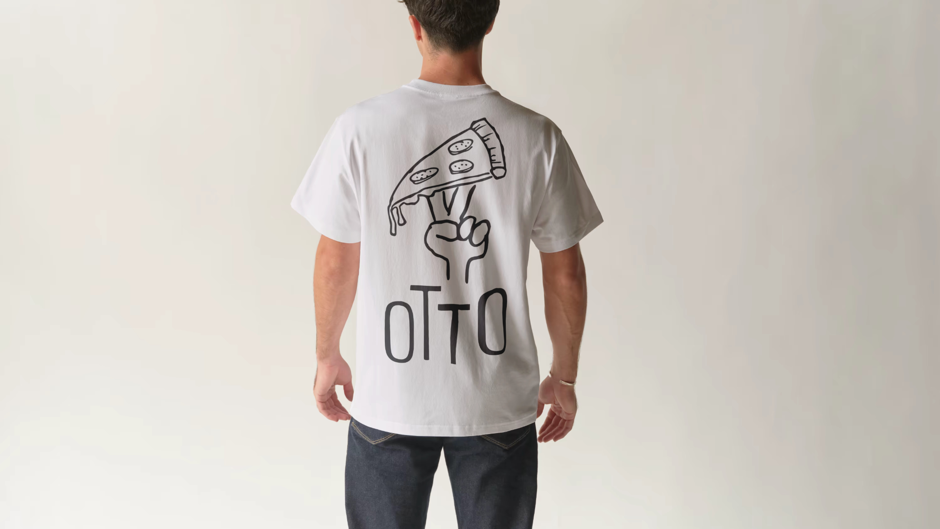 Person viewed from behind wearing a white T-shirt with a black line drawing of a pizza slice held by a hand and the word 'OTTO' below.