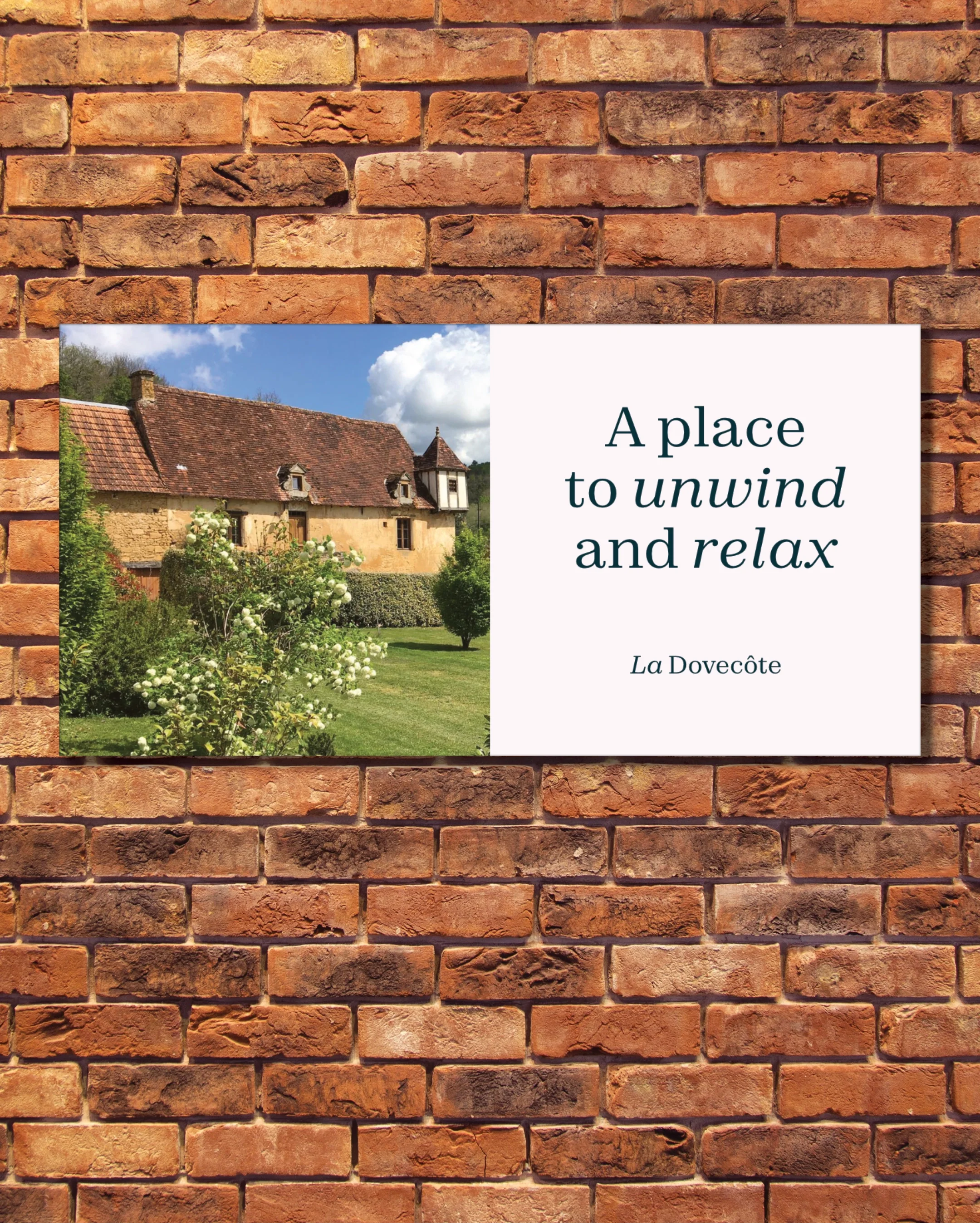 A sign on a brick wall with a photo of a rustic house and garden. The sign reads 'A place to unwind and relax. La Dovecôte.'