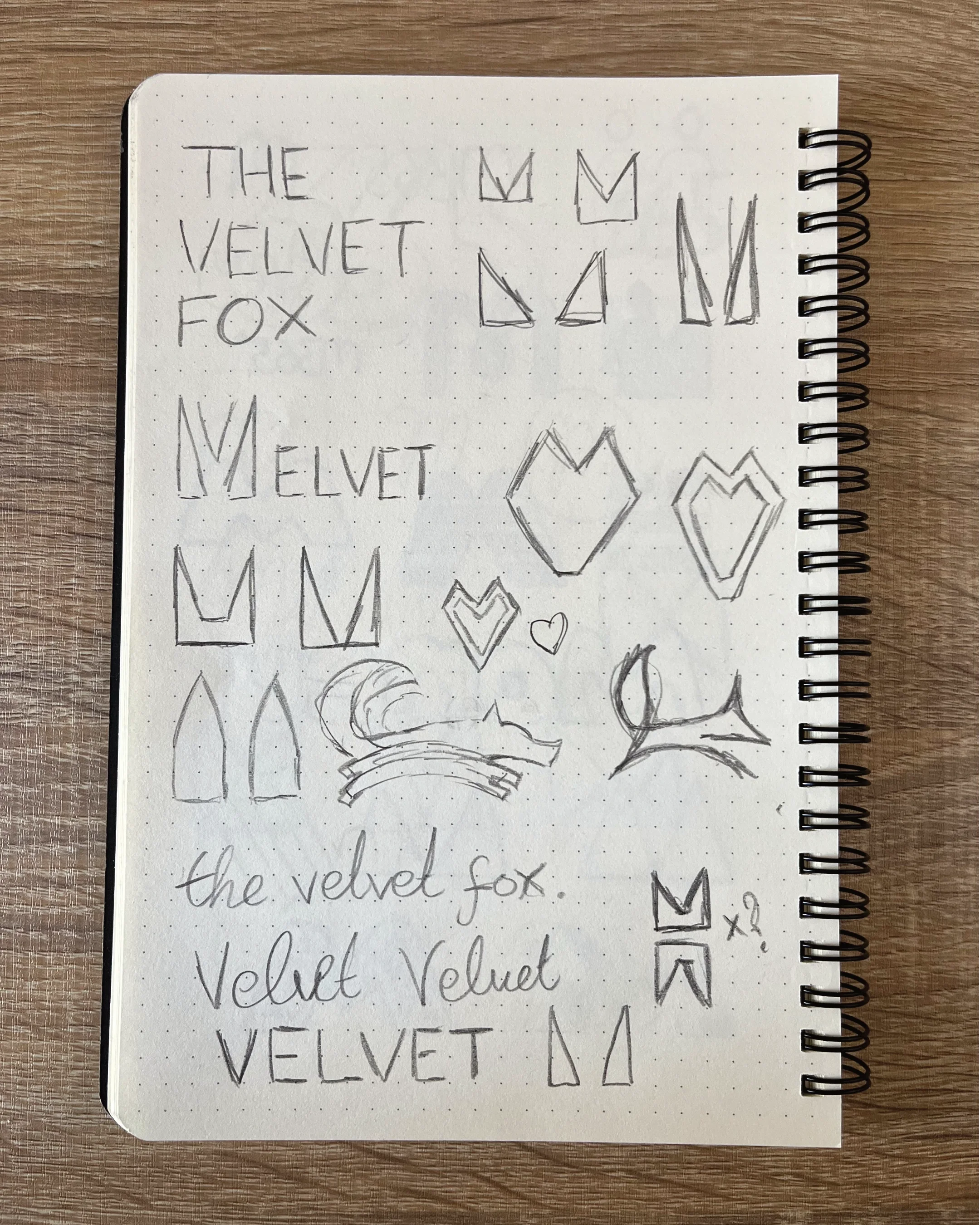 Sketches of various crown and heart shapes, handwritten words 'The Velvet Fox' and 'Velvet' on dotted notebook paper.