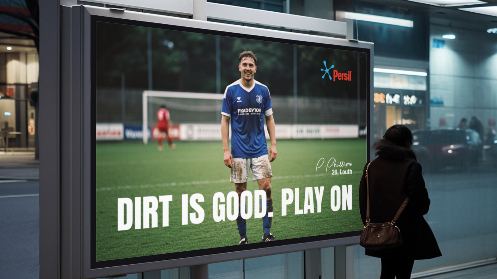 Billboard advertisement featuring a male soccer player in a blue jersey on a grassy field. The text on the billboard reads 'Dirt is good. Play on' and includes the name P. Phillips, 26, Louth. A person with a backpack stands in front of the billboard