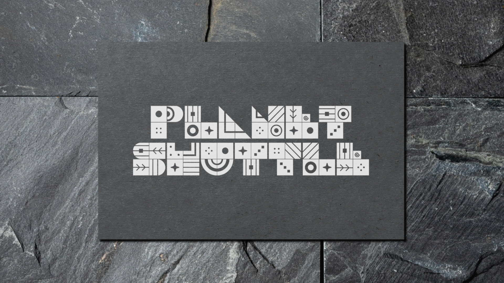 A black tile with the phrase "POLY FEST" written in white, composed of various geometric shapes and symbols, placed on a textured stone surface.