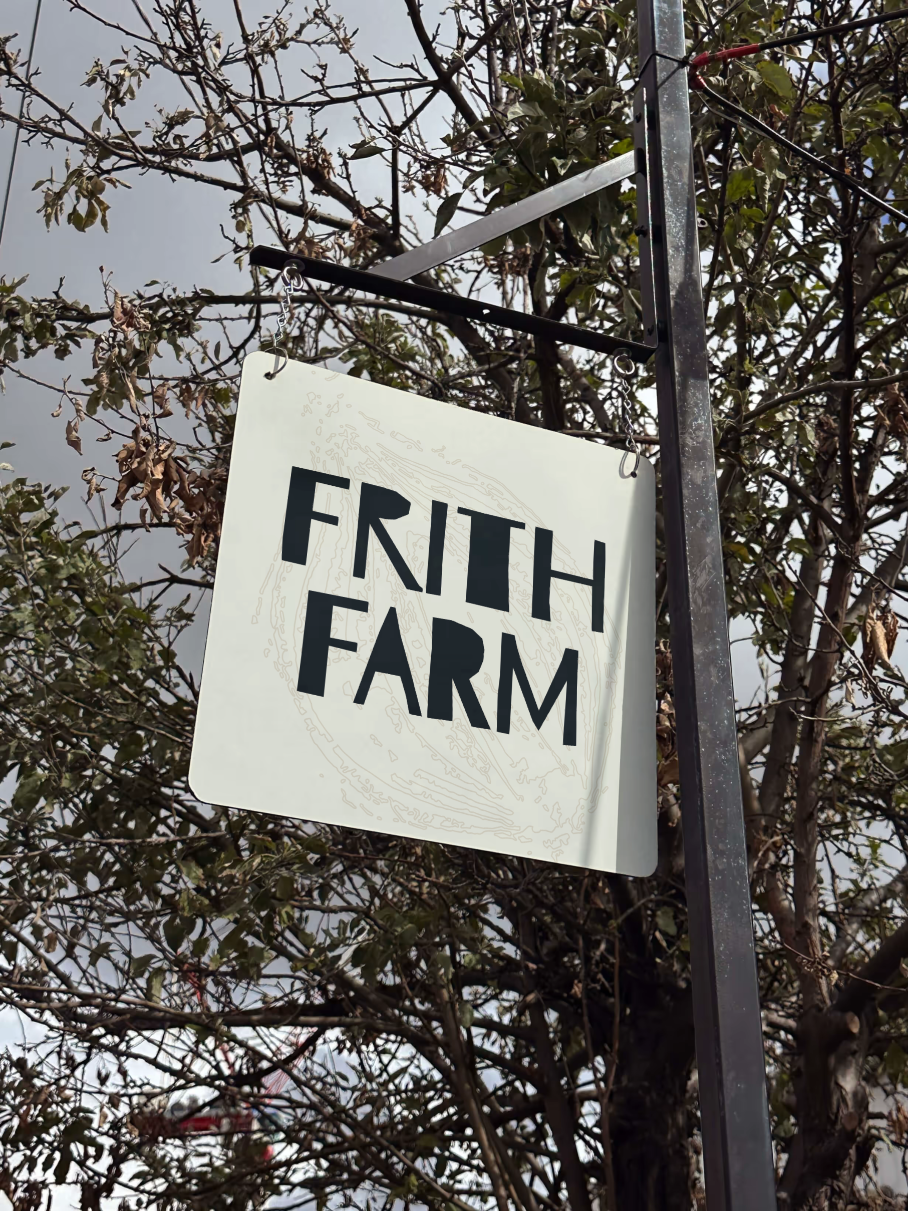 A sign reading 'FIRTH FARM' hanging from a black metal frame, with a backdrop of autumn leaves on trees and a cloudy sky.
