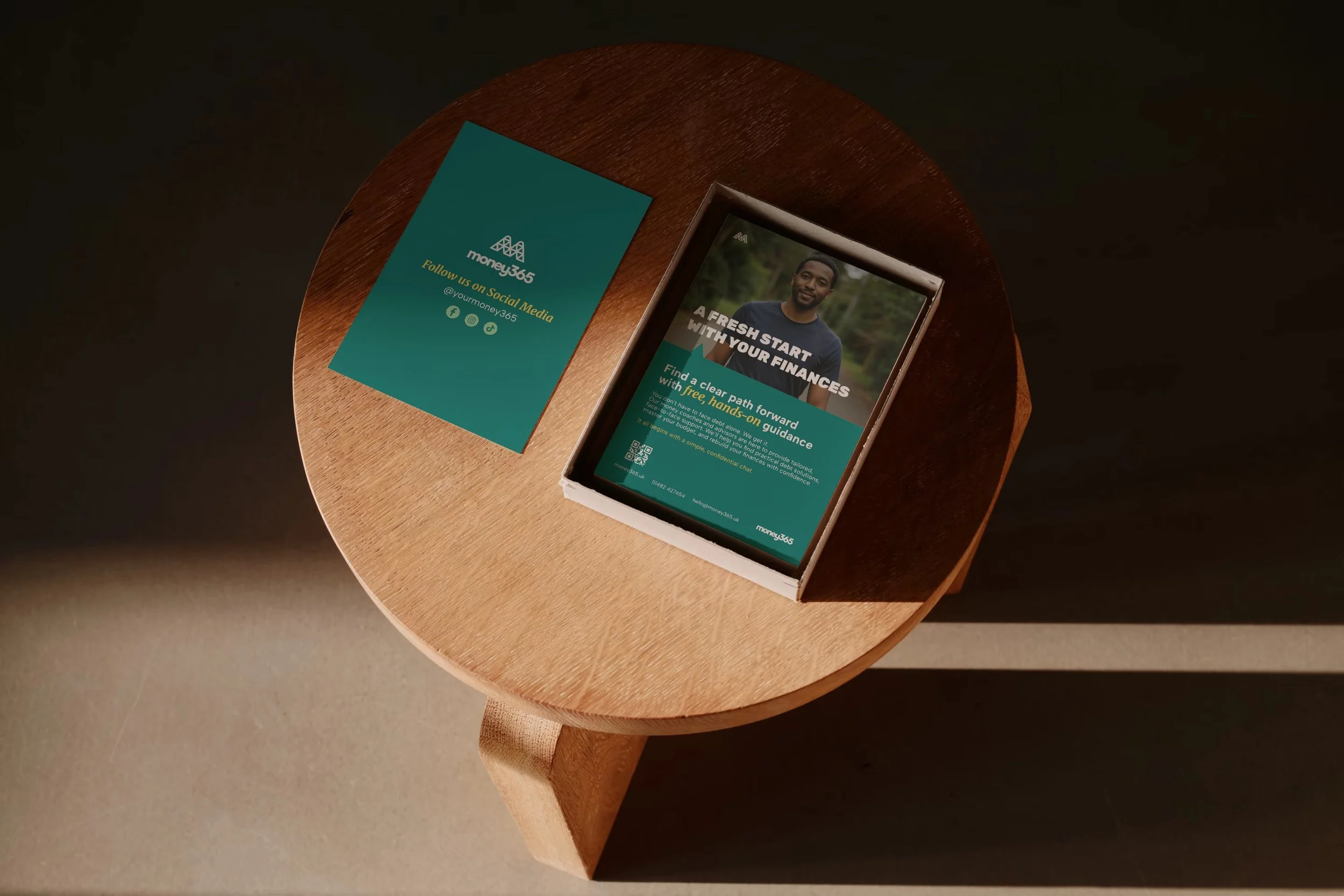 Box of Money365 branded leaflets in a box sat on a wooden coffee table