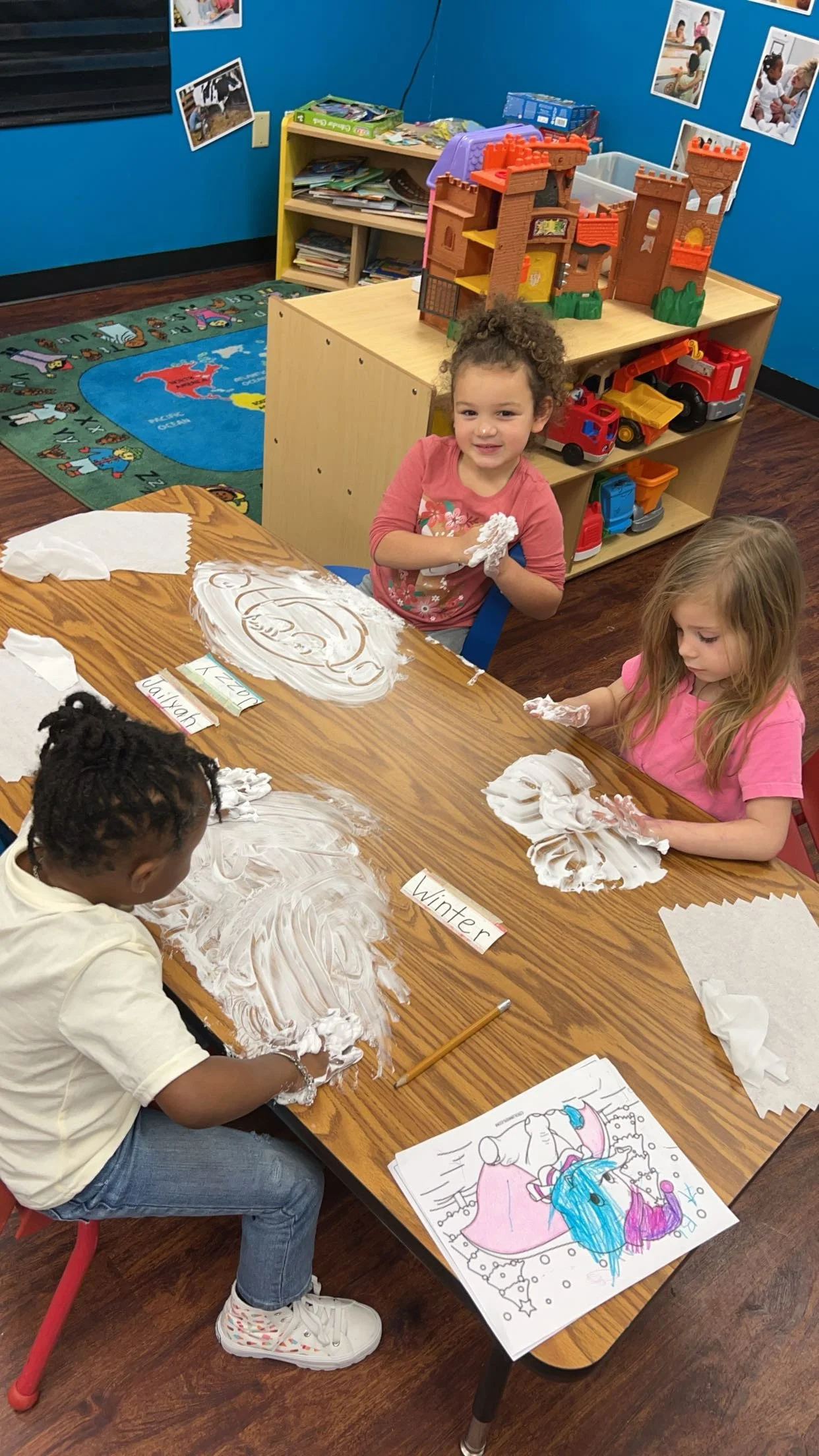 Children playing with shaving cream on a table in a classroom.