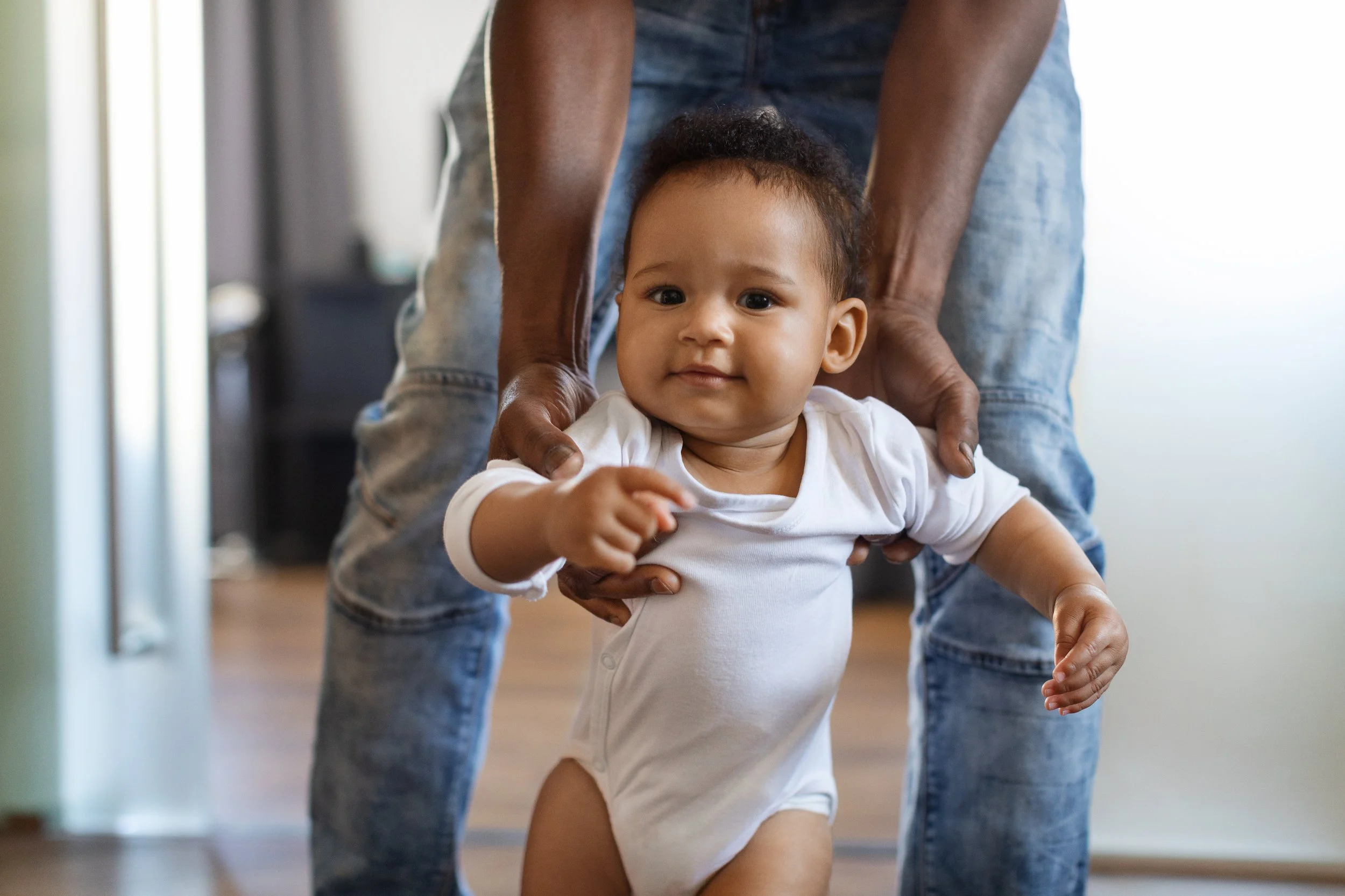 Baby in white onesie being held while walking indoors