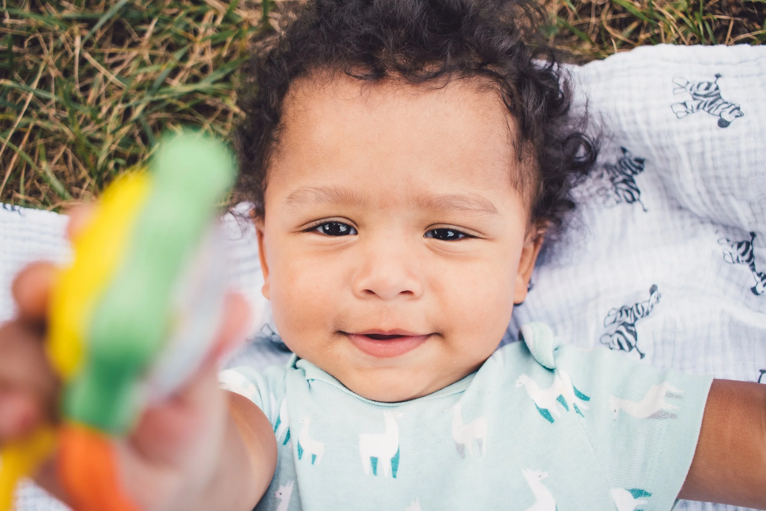 Smiling baby lying on a blanket, holding a colorful toy.