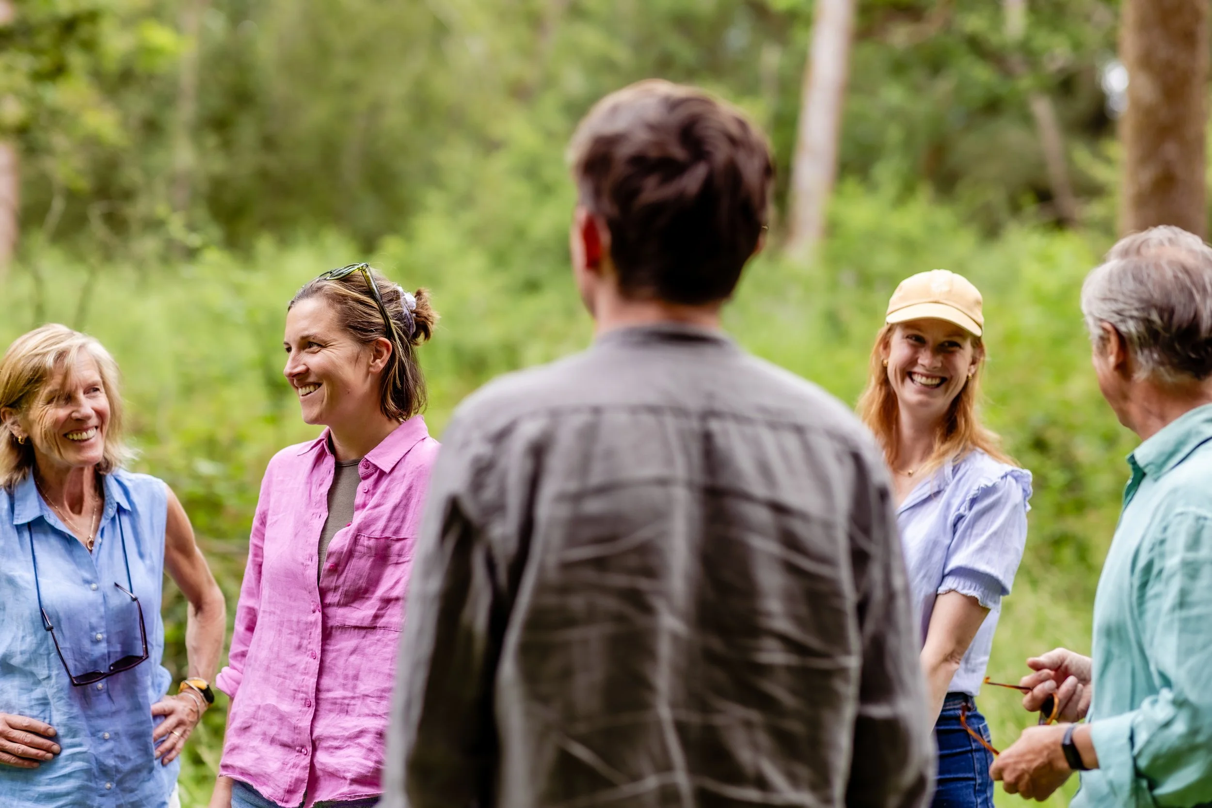 Group of people outdoors in a green forest, smiling and engaging in conversation.