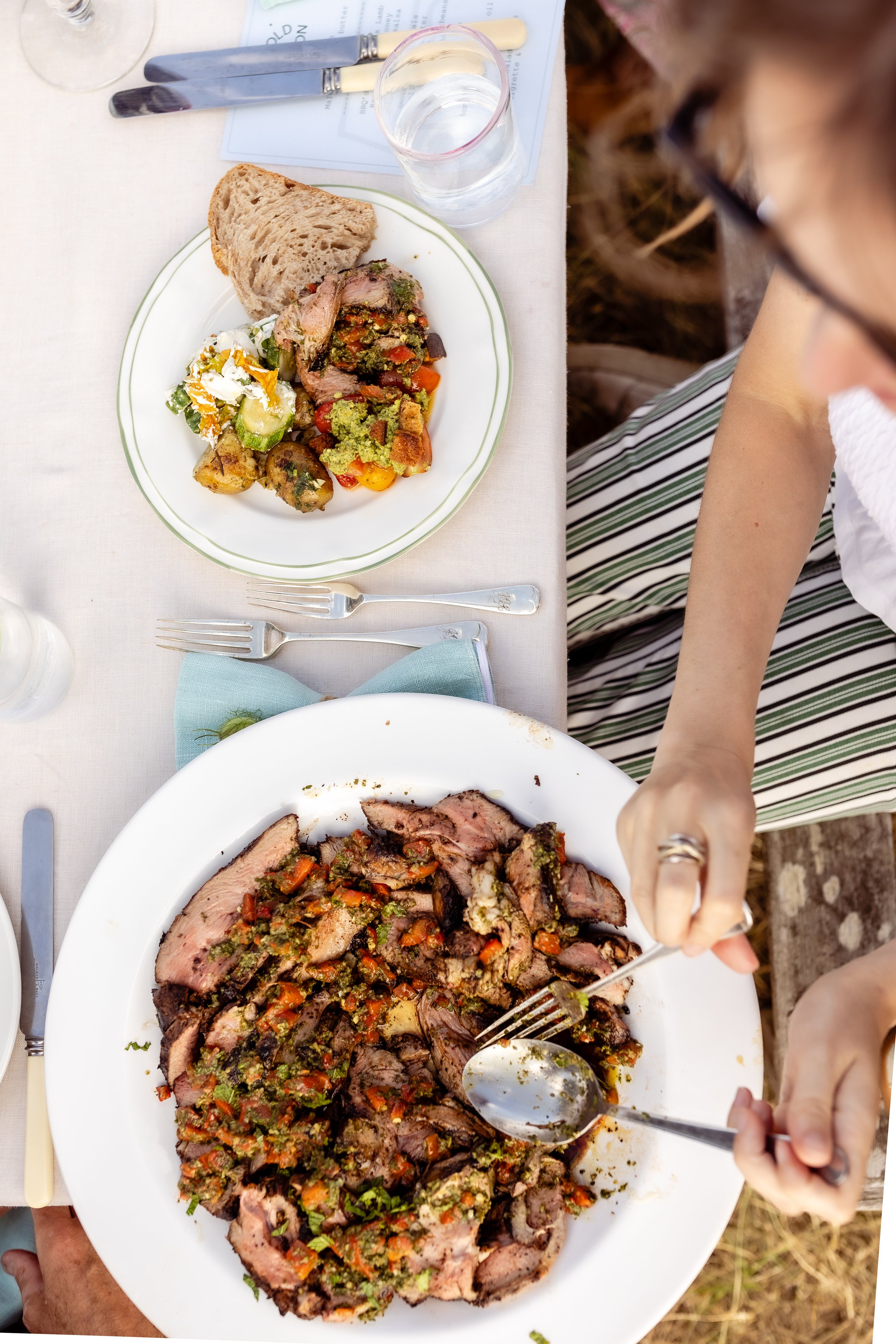 Person carving a stuffed meat roast with vegetables on a white plate at a dinner table.