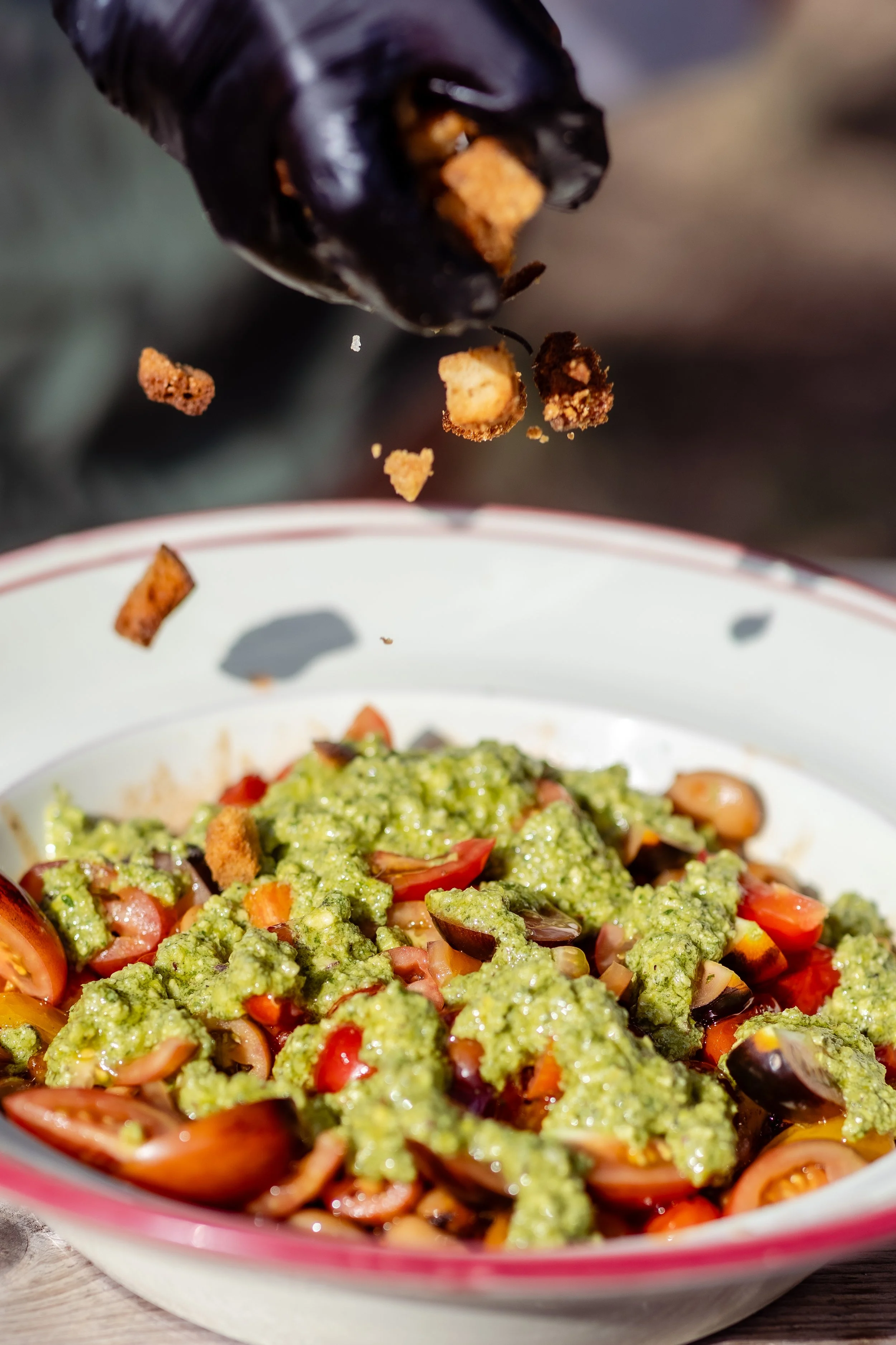 Close-up of a bowl of chopped tomato, avocado, and black olives with guacamole on top, with crumbled tortilla chips falling into the bowl.