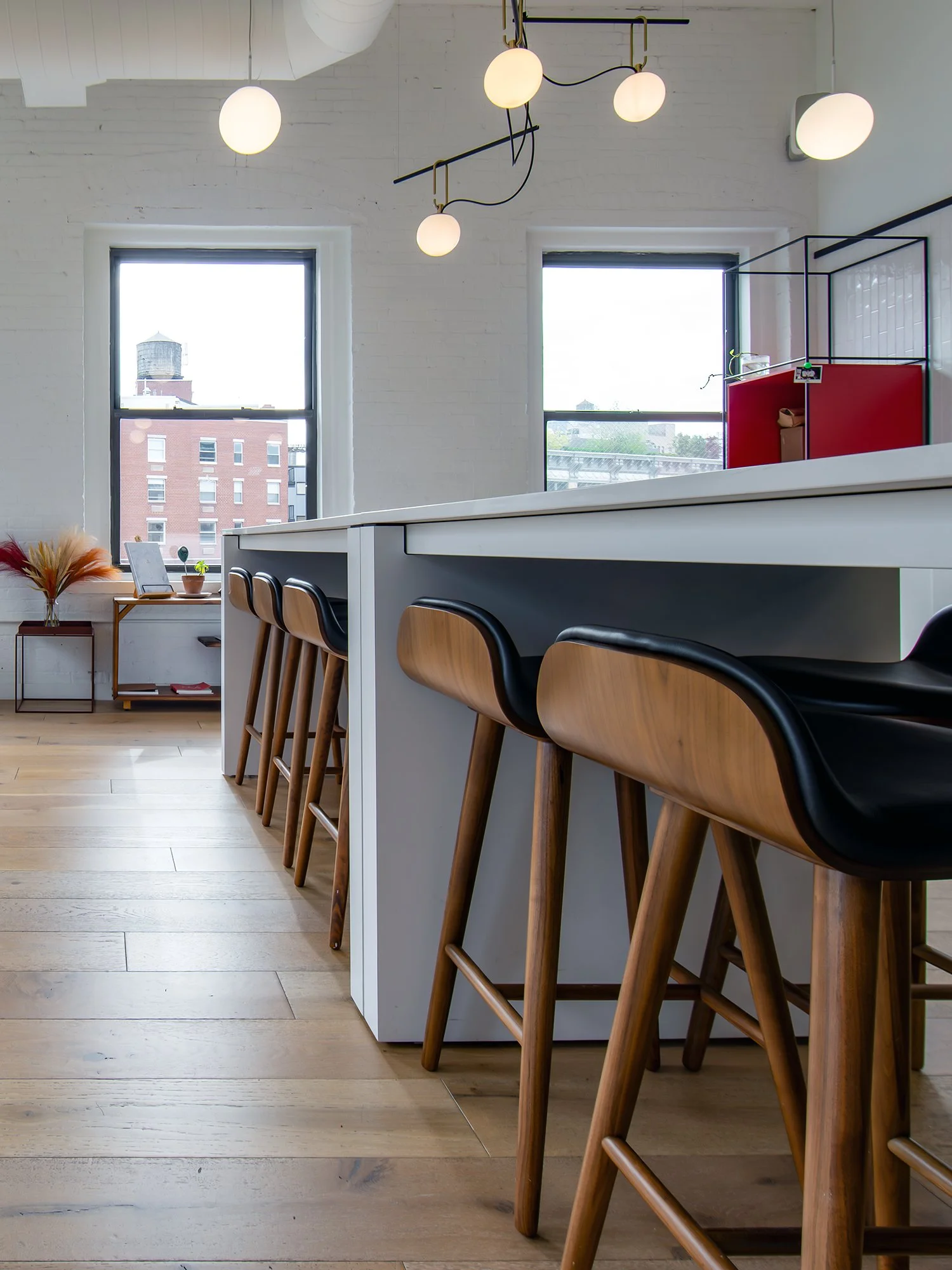 Modern kitchen with a white island counter and wooden bar stools, large windows, and contemporary lighting fixtures.