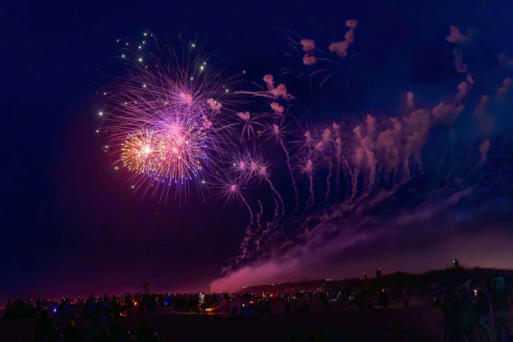 Night sky filled with colorful fireworks, with a crowd of people watching from the ground