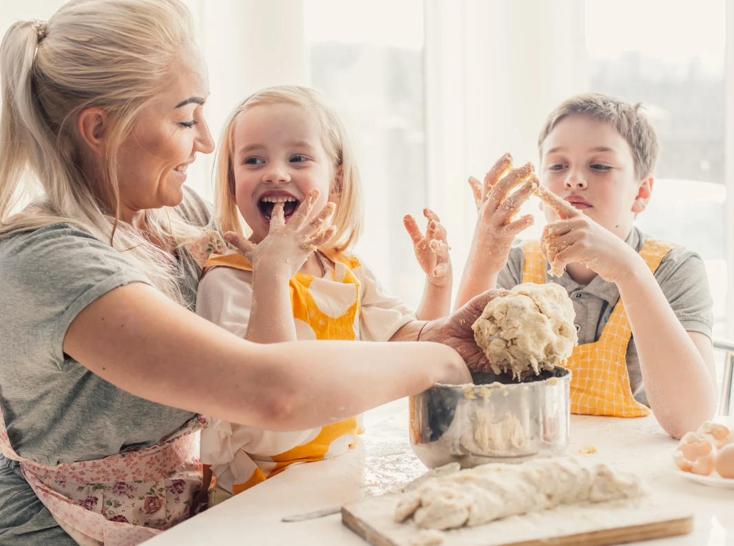 A woman and two children making bread together in a bright kitchen.