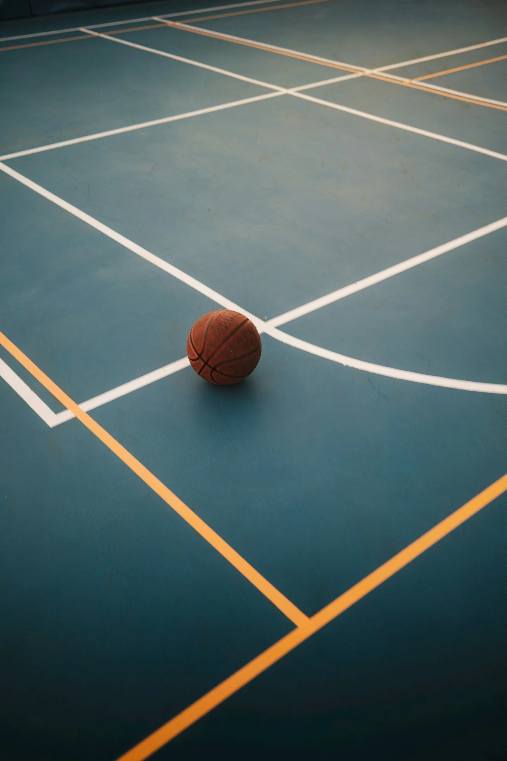A basketball on a blue indoor court with white and yellow court lines.