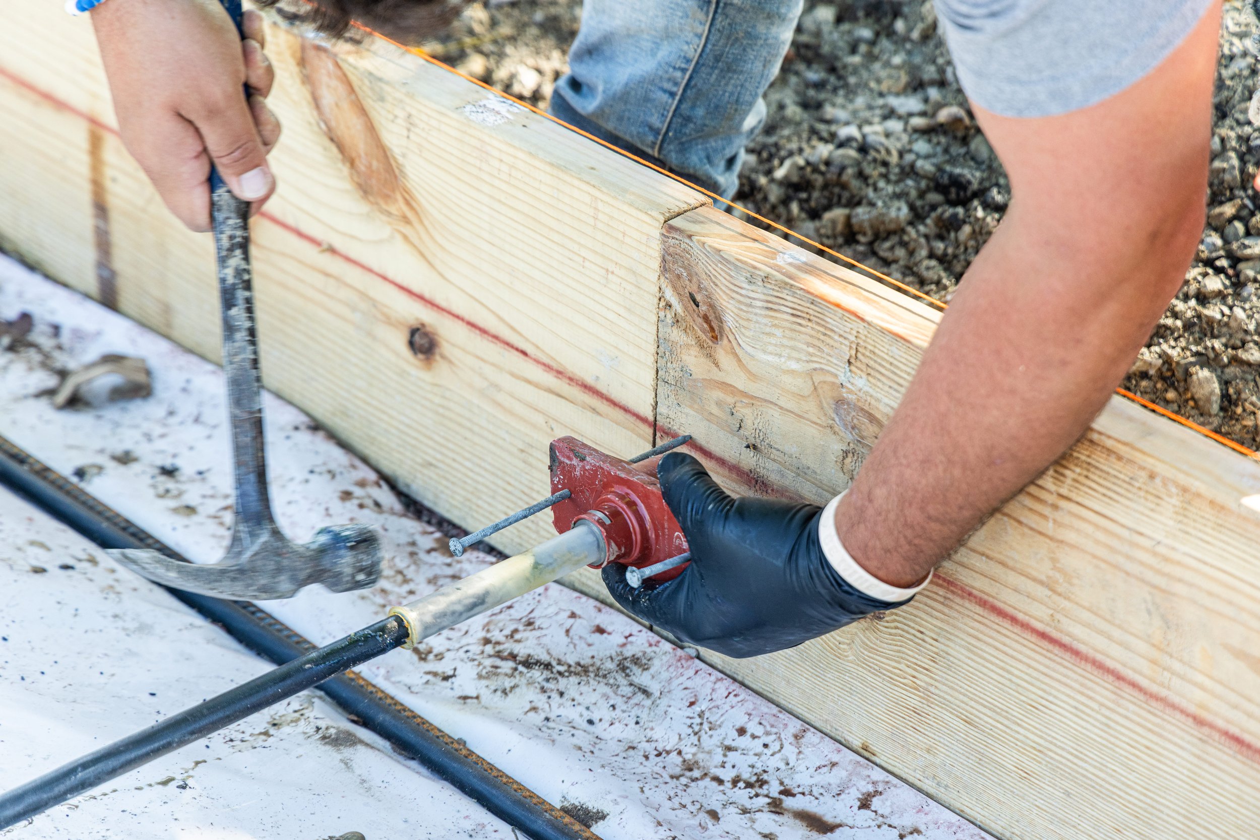 Person using a tool to secure a wooden beam at a construction site, with one hand wearing a black glove.