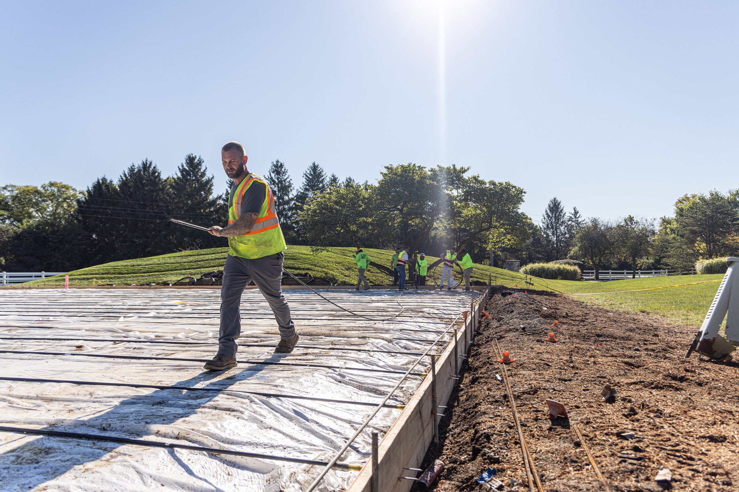 Workers installing a concrete slab on a construction site outdoors on a sunny day, with trees in the background.
