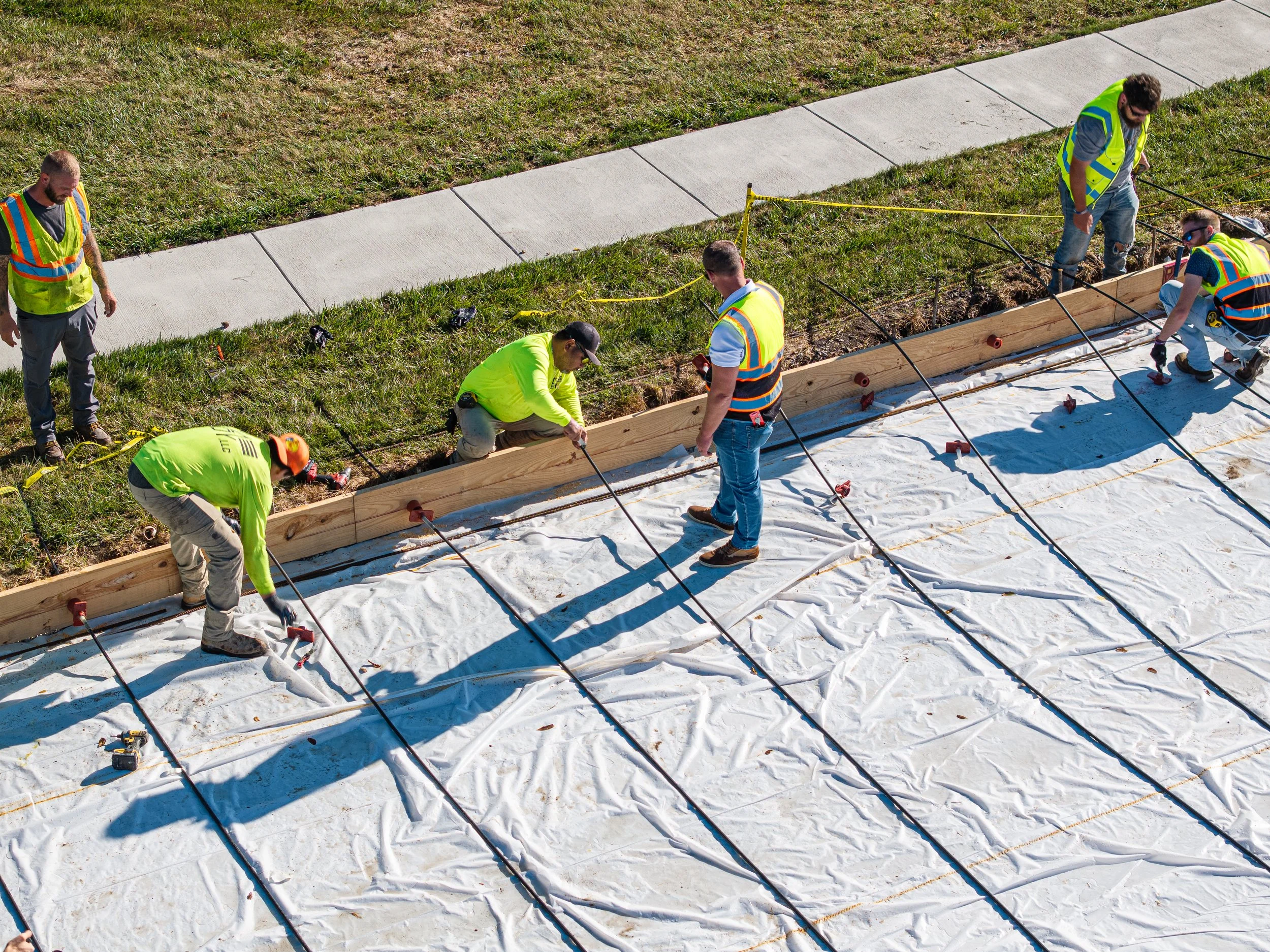 Workers laying down insulation and preparing a foundation for construction, wearing safety vests and gloves.