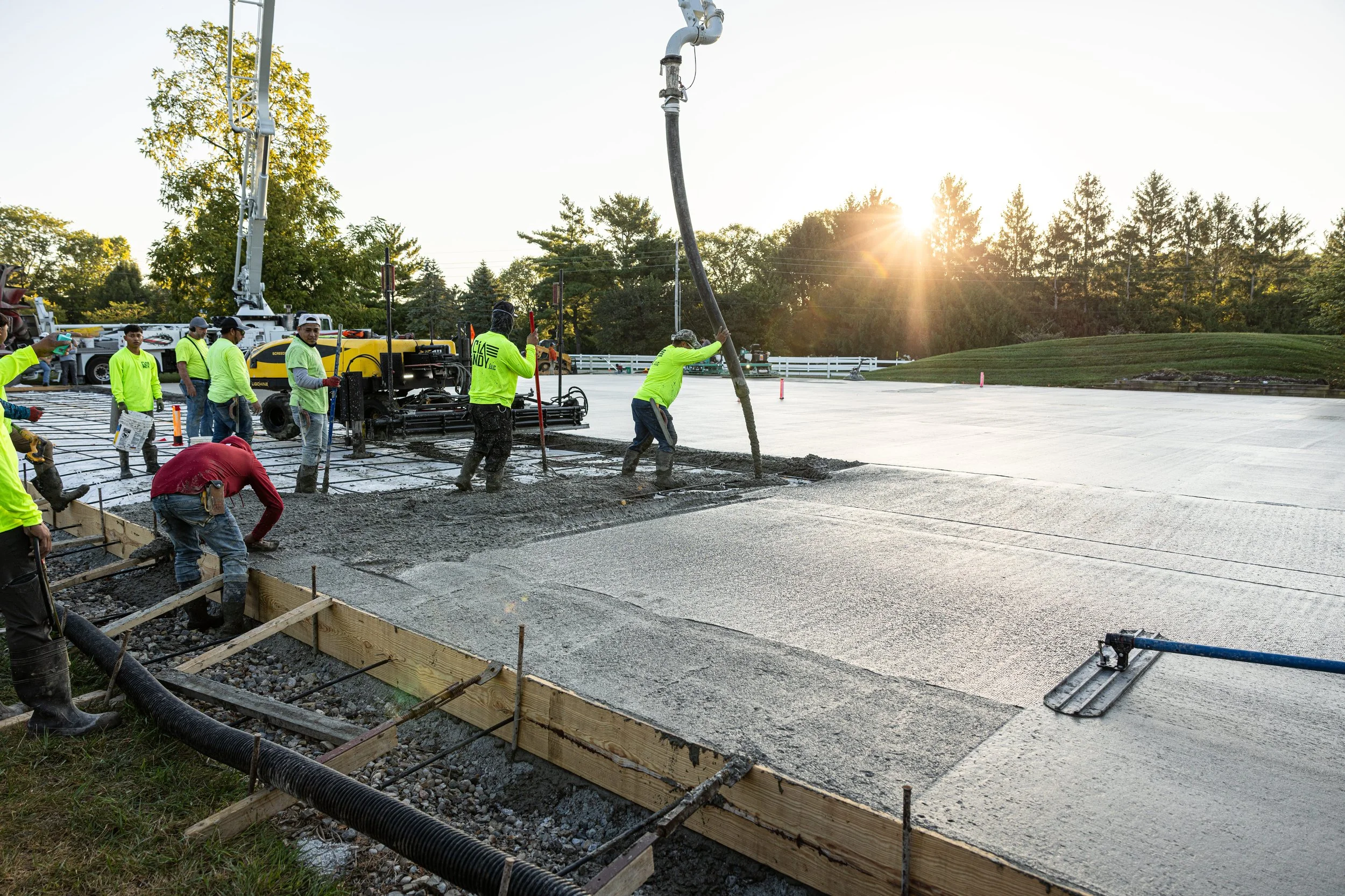 Construction workers laying concrete pavement outdoors at sunset.