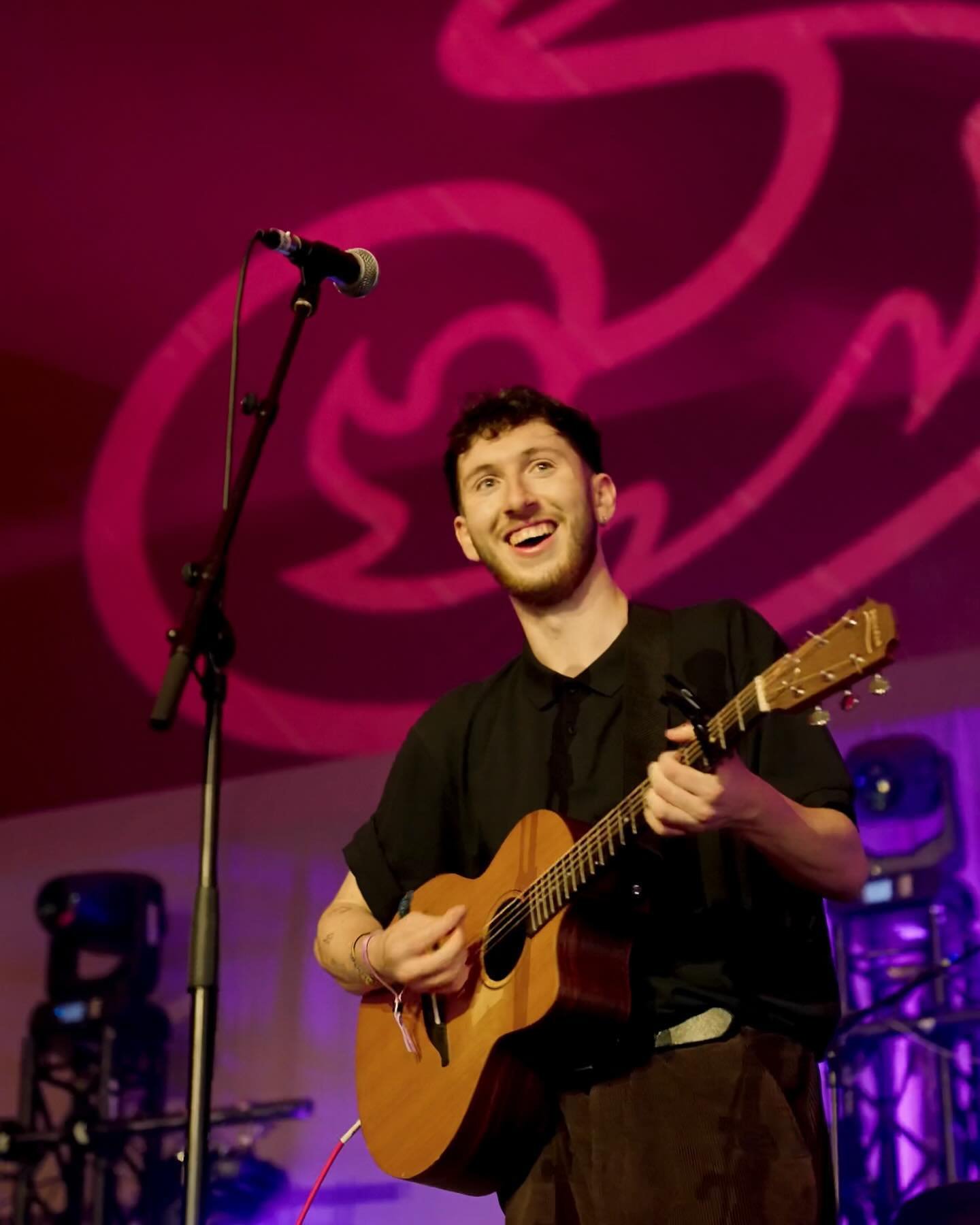 A musician performing on stage with a guitar under purple lighting.