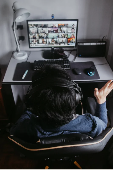 Person wearing headphones, participating in a video conference on a desktop computer, seen from behind.