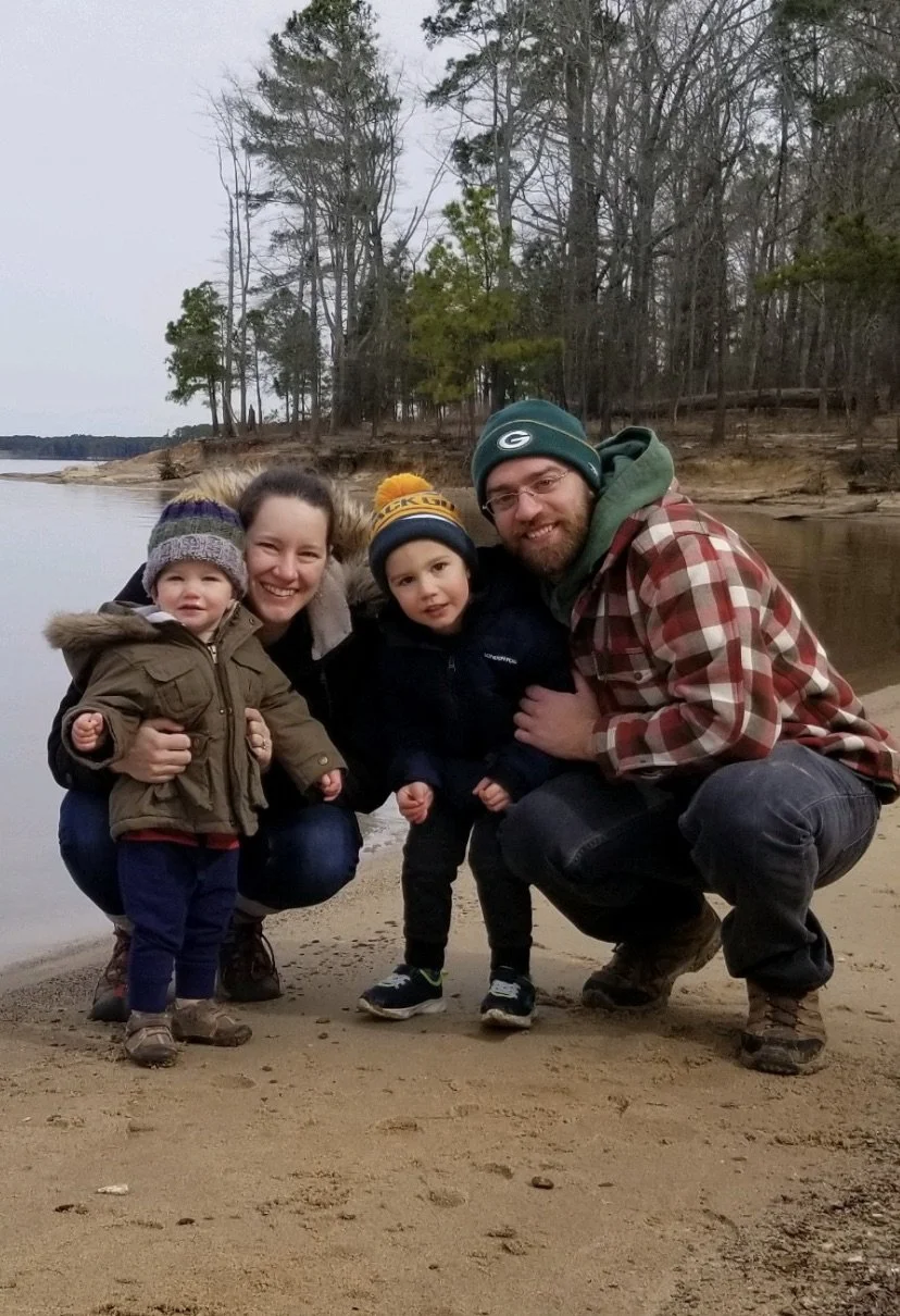 Family on a sandy beach with trees in the background, smiling at the camera.