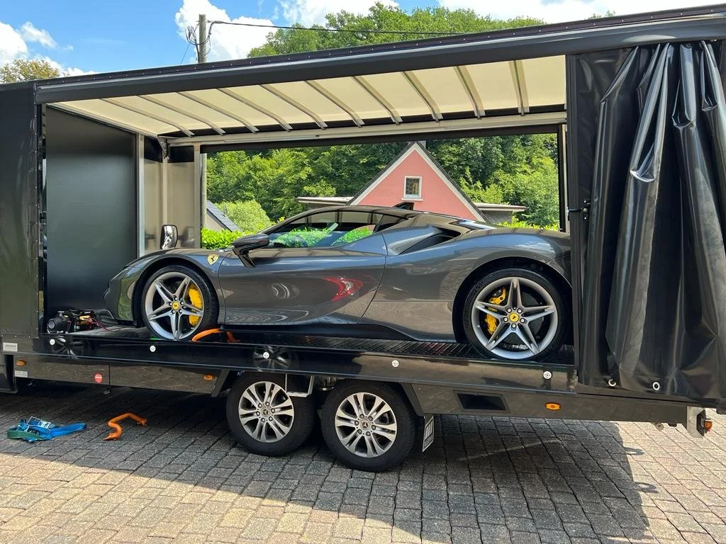 Ein grauer Ferrari Sportwagen auf einem Transportanhänger, der im Freien steht.