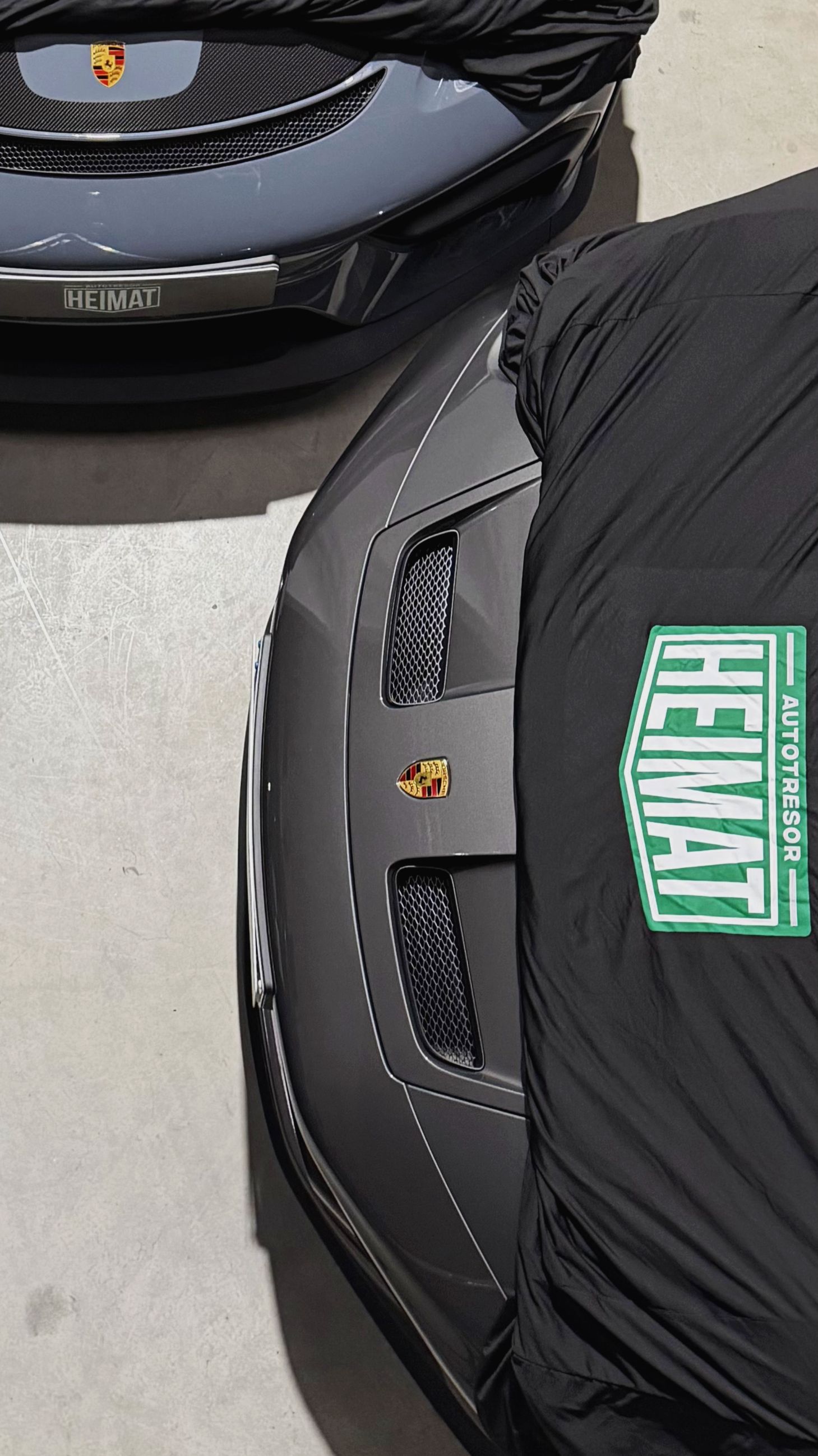 Nahaufnahme von zwei Porsche Fahrzeugen. Die Autos sind teilweise von einem Carcover bedeckt.
