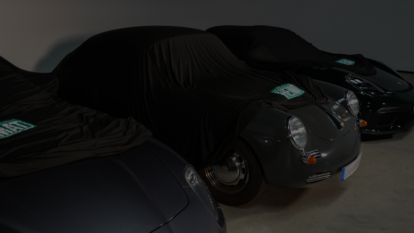 Drei unter einem Carcover versteckte klassische Porsche-Sportwagen in einem dunklen Raum.