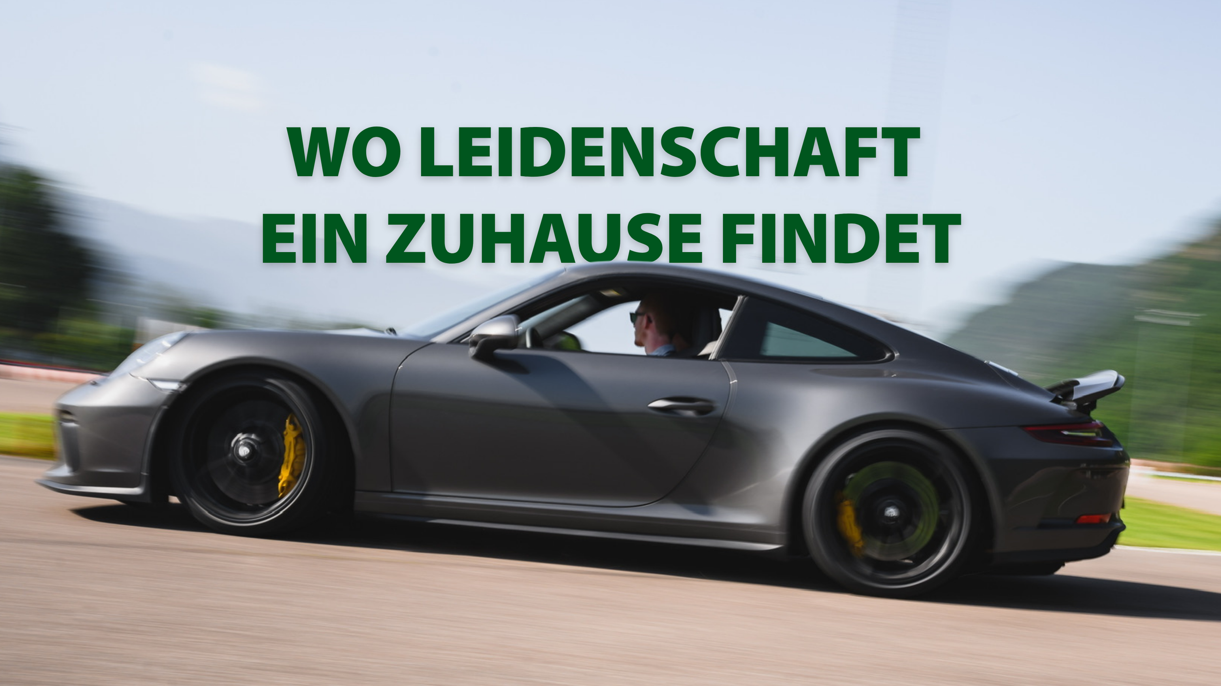 Ein grauer Sportwagen fährt schnell auf einer Straße, mit grünen Bäumen im Hintergrund. Der Text "Wo Leidenschaft ein Zuhause findet" ist in grüner Schrift über dem Auto sichtbar.