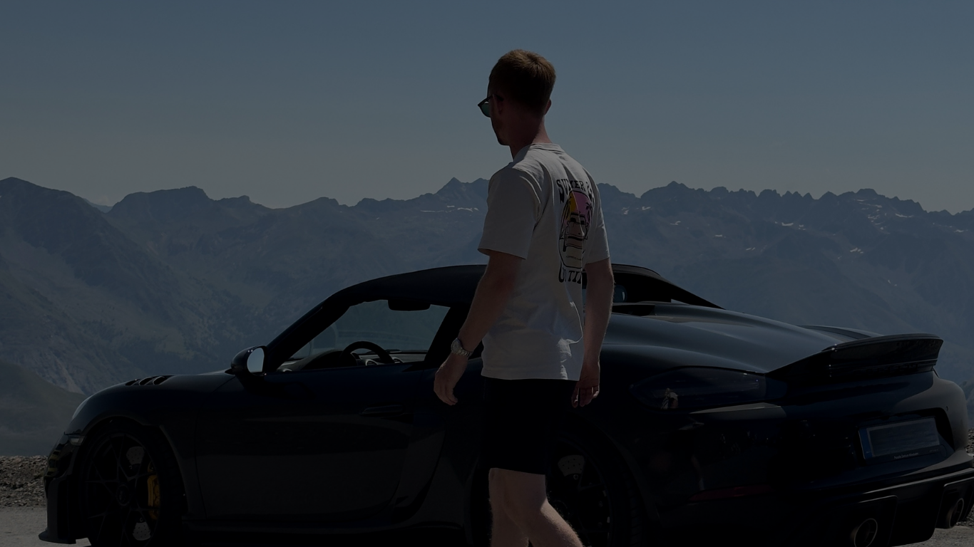 Mann steht neben einem grünen Sportwagen in den Bergen bei Sonnenschein.